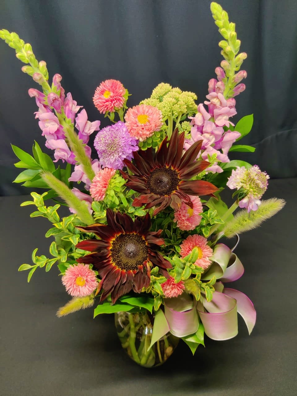Mixed bouquet with dark sunflowers, pink blooms, and a glass vase