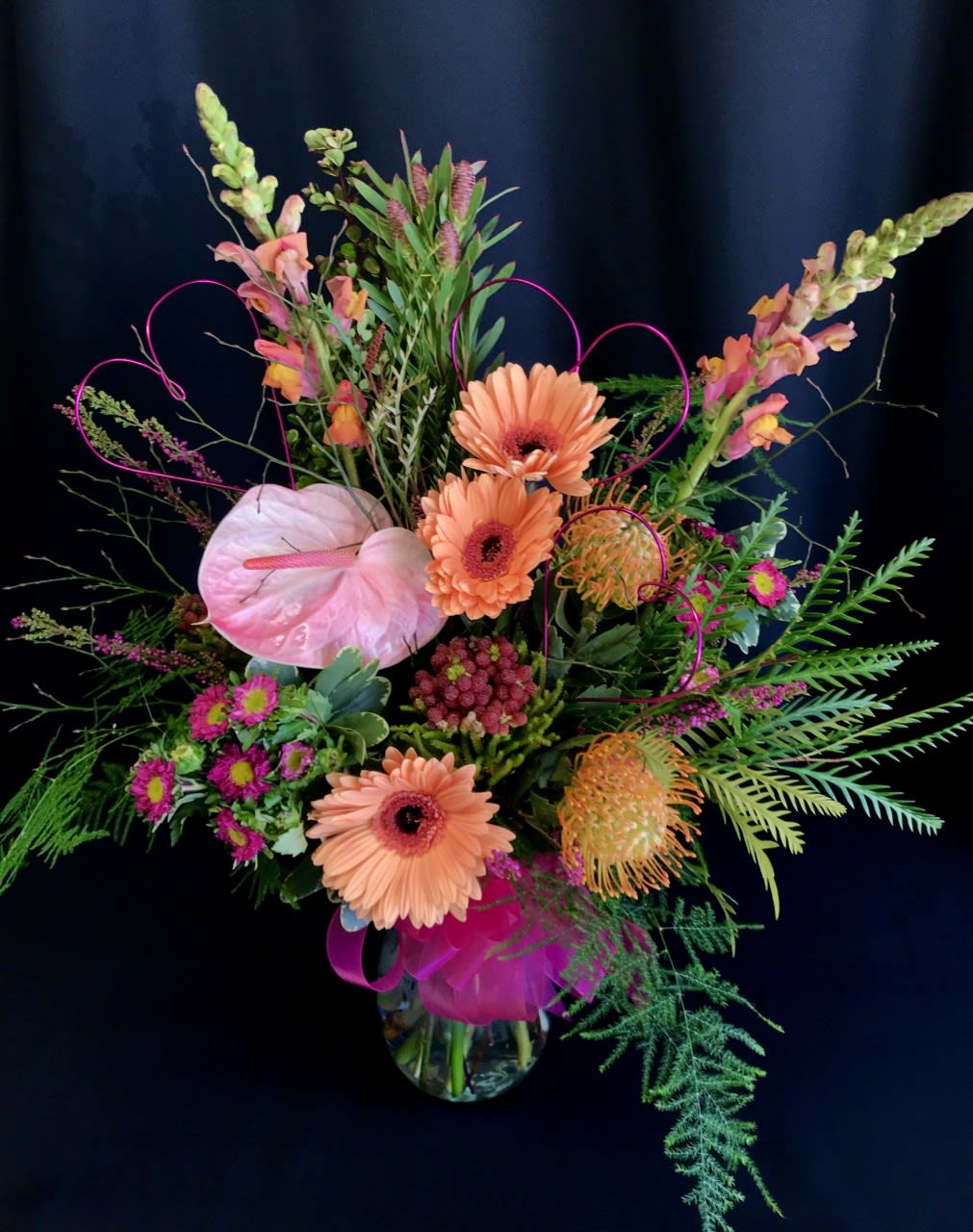 Colorful floral arrangement with pink anthurium and peach gerbera daisies in a glass vase