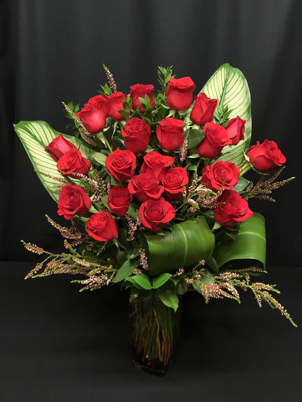 Bouquet of red roses with broad green leaves in a glass vase
