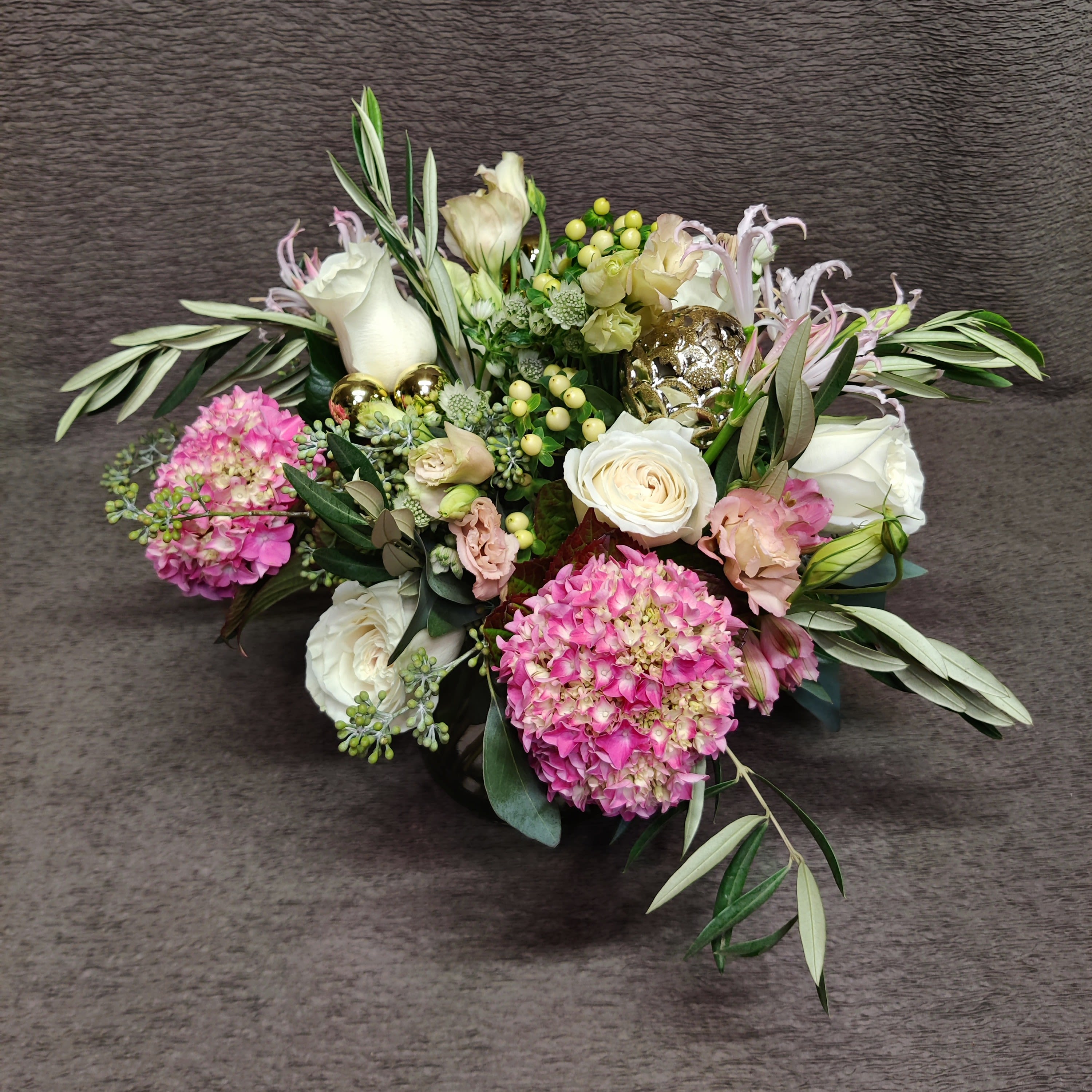 Pink Winter Center;piece with Ornaments - All the splendor of the holiday season: plump hydrangea and lisianthes, berries, shiny ornaments and accents and rustic olive branches.*  Set the tables at your winter holiday event with our lovely natural centerpieces.