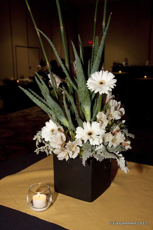 White gerbera daisies and pale flowers in a black vase with tall spiky foliage
