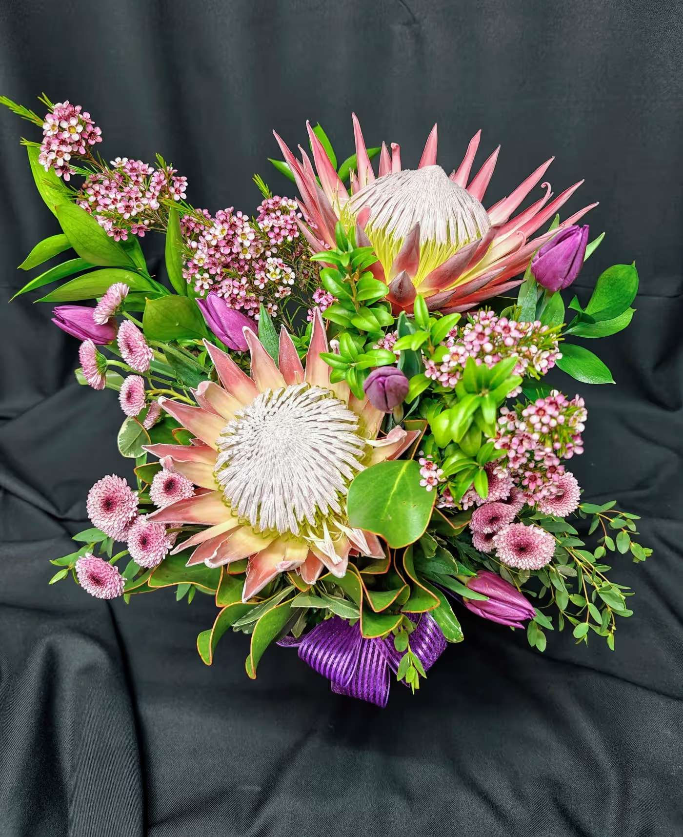 Pink and white protea bouquet with purple buds and green foliage