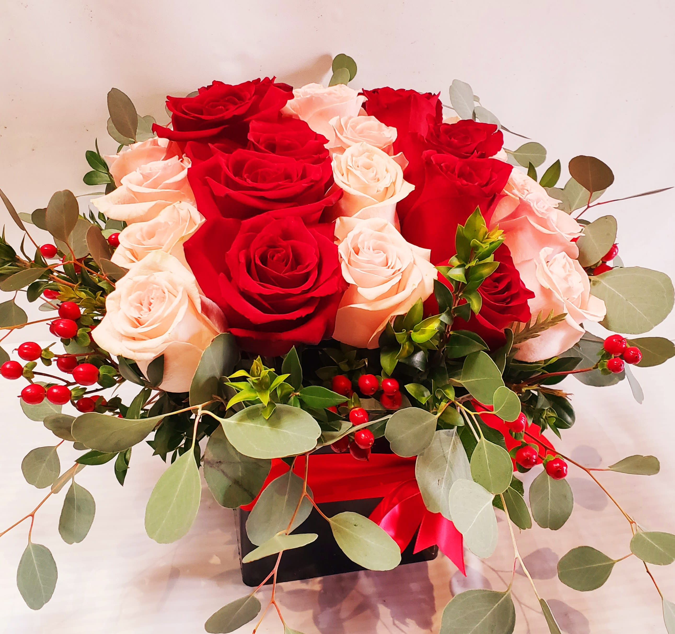 Red and blush roses arranged in a black box with eucalyptus and red berries