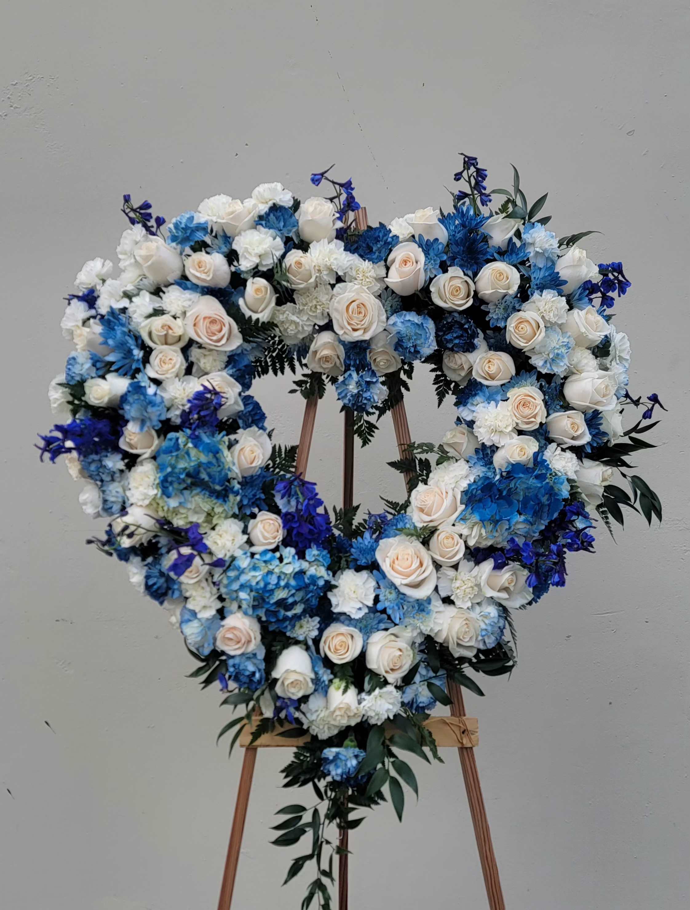 Heart-shaped floral wreath of white and blue roses on an easel