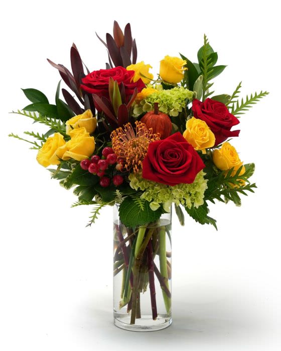 Tall arrangement of red and yellow roses with green hydrangea in a clear glass vase