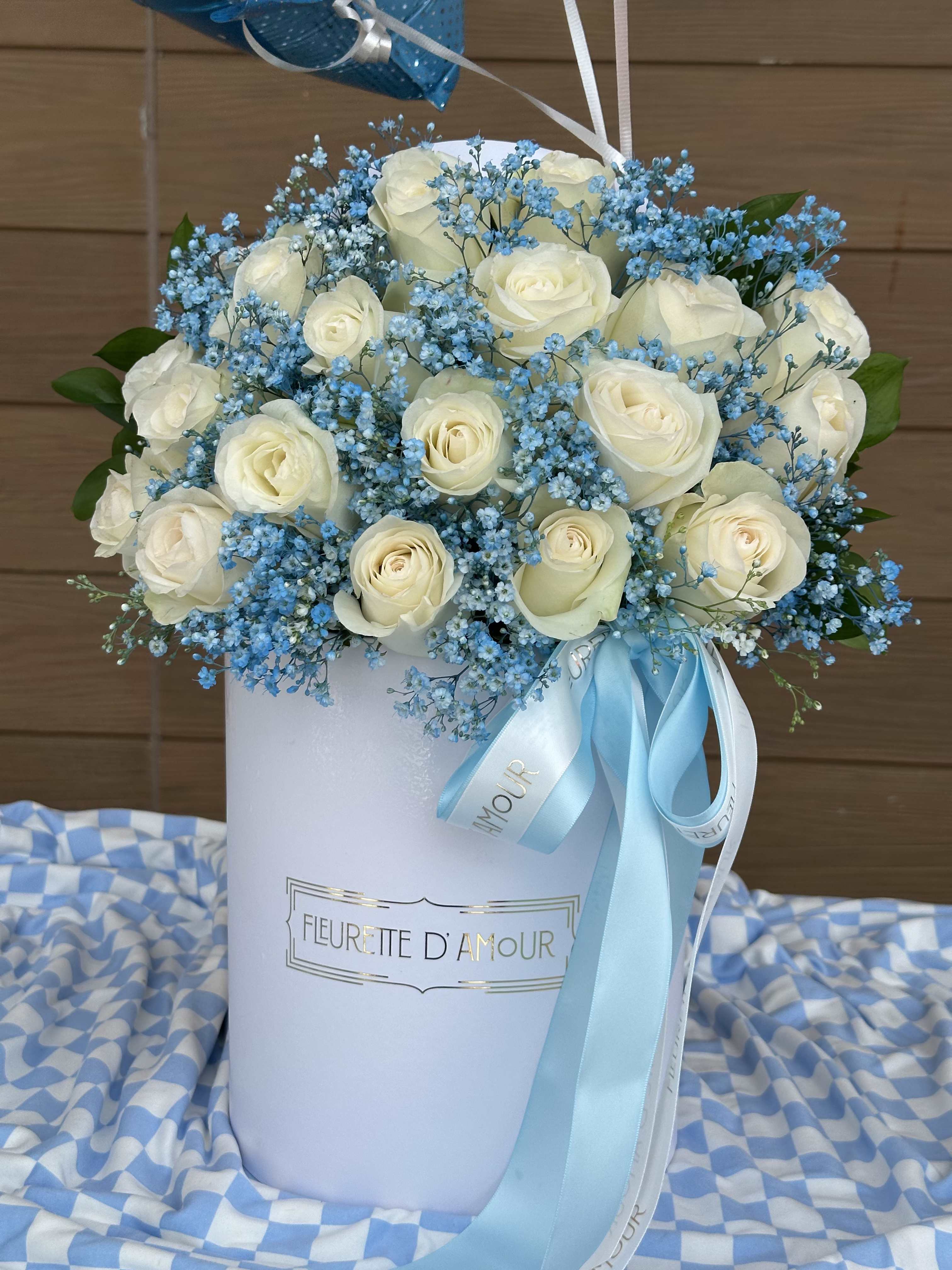 White roses and blue baby's breath in a white hatbox with ribbon