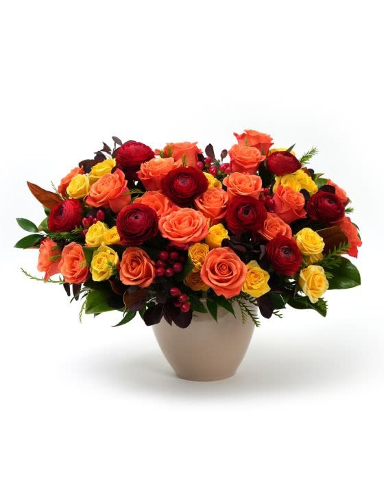 Low vase arrangement of orange, red, and yellow roses with dark red blooms