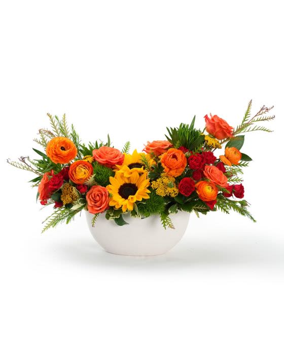 Low centerpiece with yellow sunflowers, orange roses, and red blooms in a white bowl.