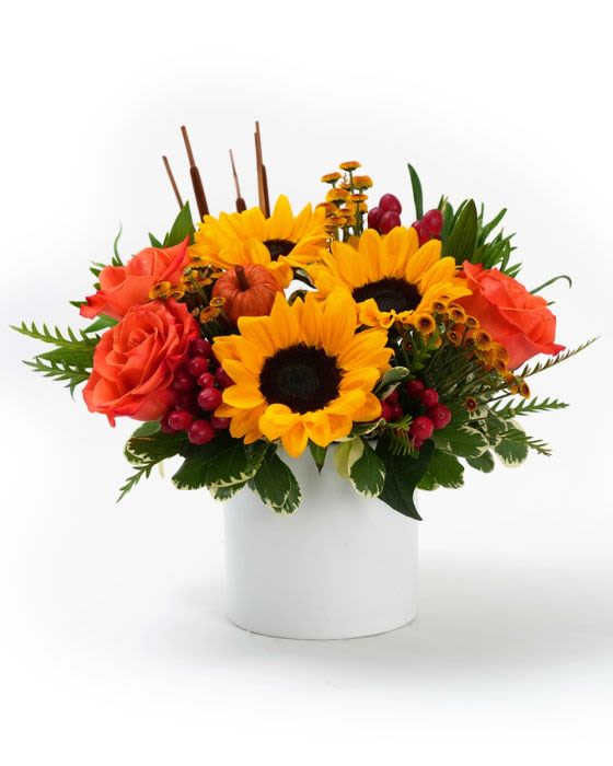 Low arrangement of yellow sunflowers and orange roses with red berries in a white vase