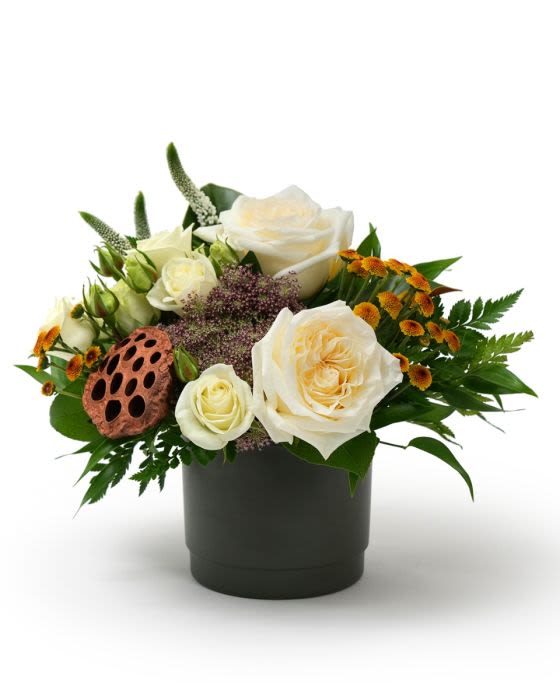 Low arrangement of ivory roses and small orange flowers in a black pot with a lotus pod accent