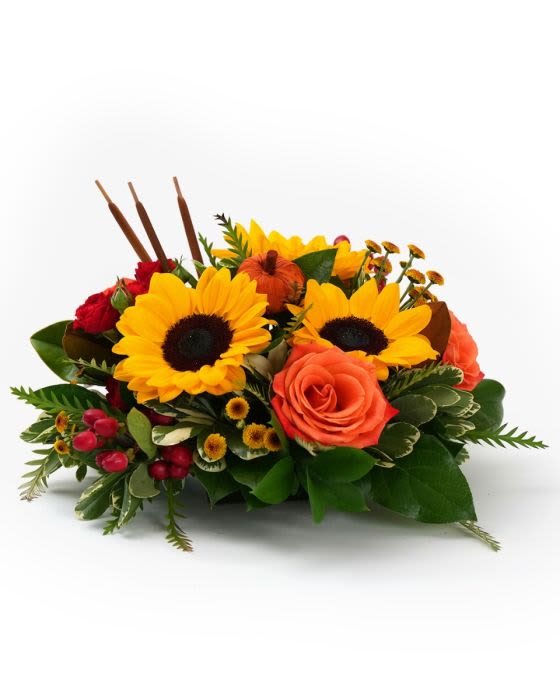 Low autumn centerpiece with bright yellow sunflowers, orange roses, red spray roses, and small pumpkins.