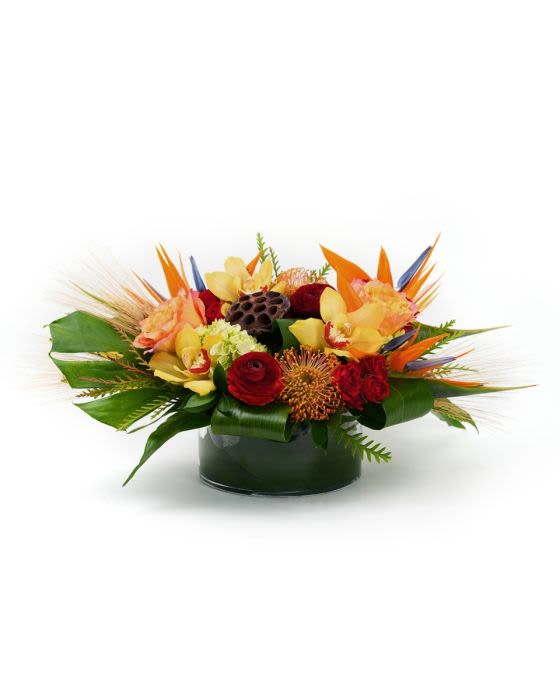 Low tropical arrangement of orange, yellow, and red flowers in a round glass vase