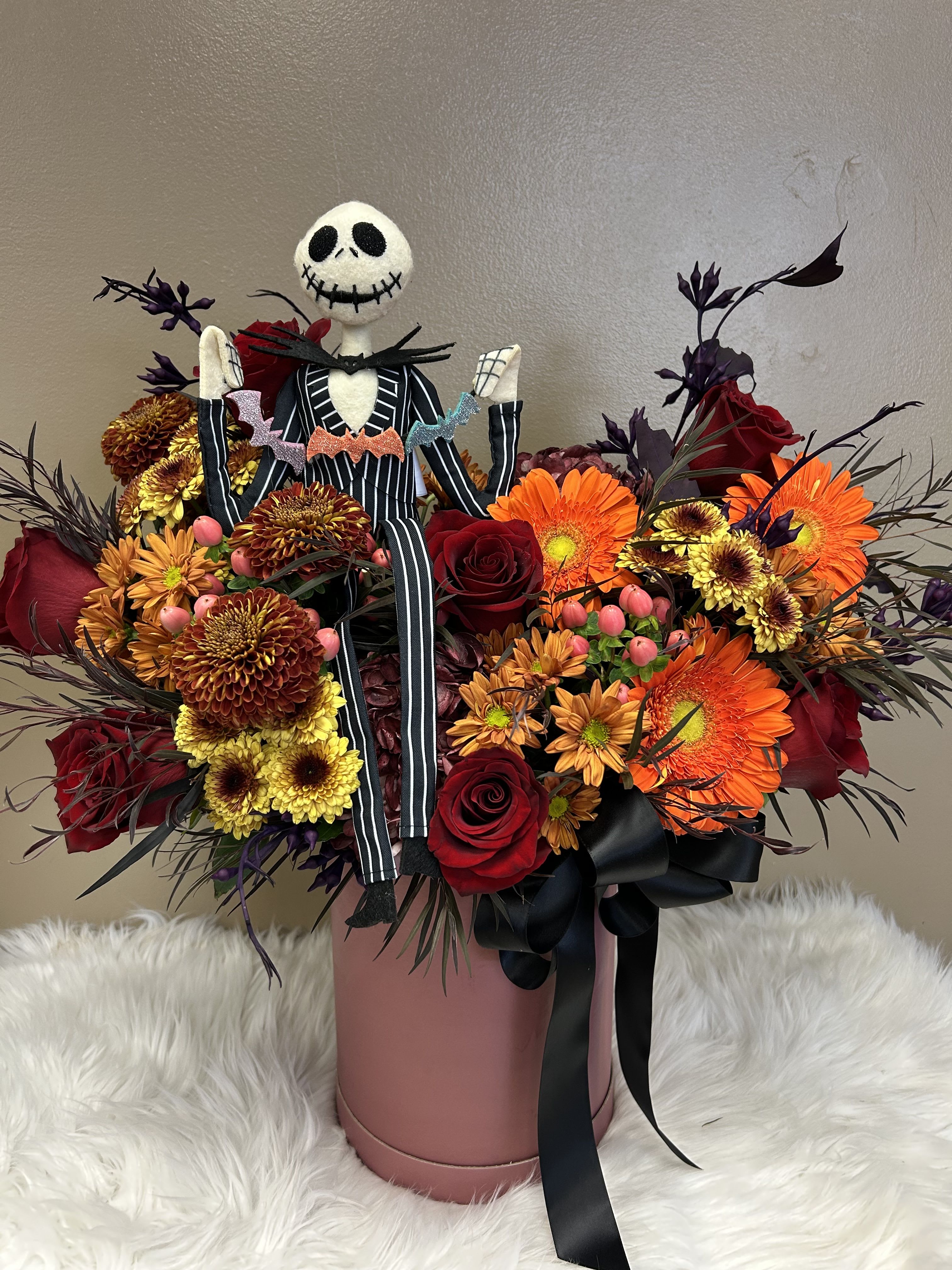 Halloween bouquet with roses, gerbera daisies, and a Jack Skellington figure in a pink box