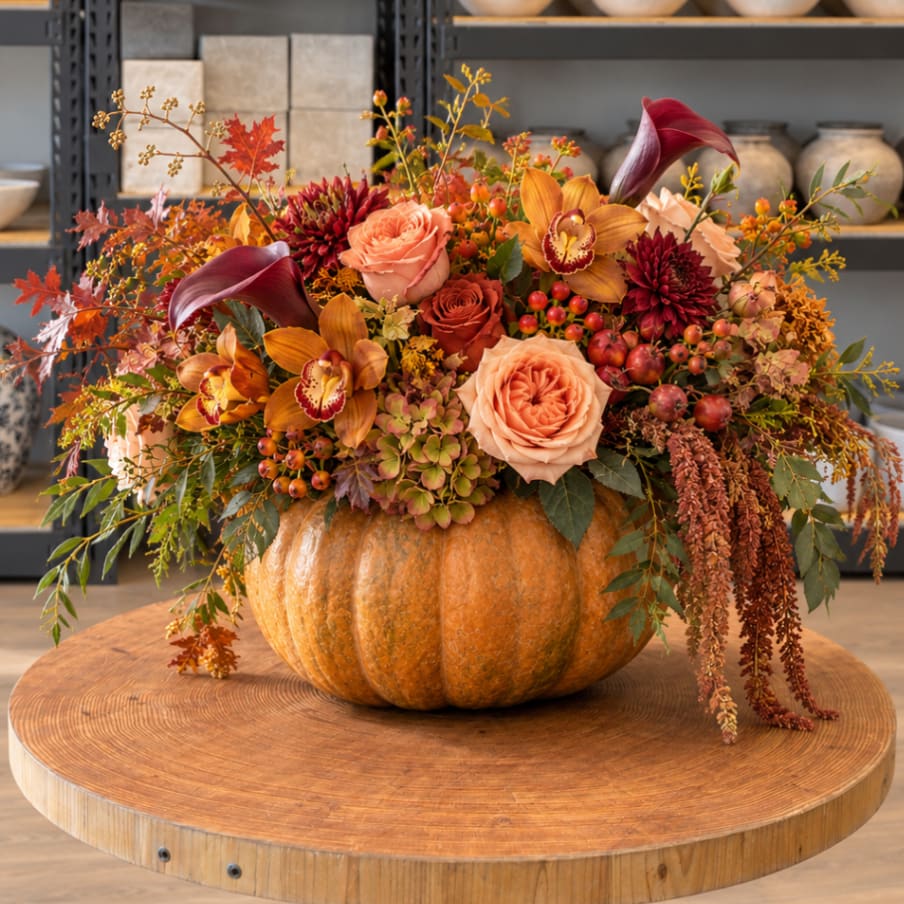 Autumn floral arrangement in a pumpkin container with roses and orchids