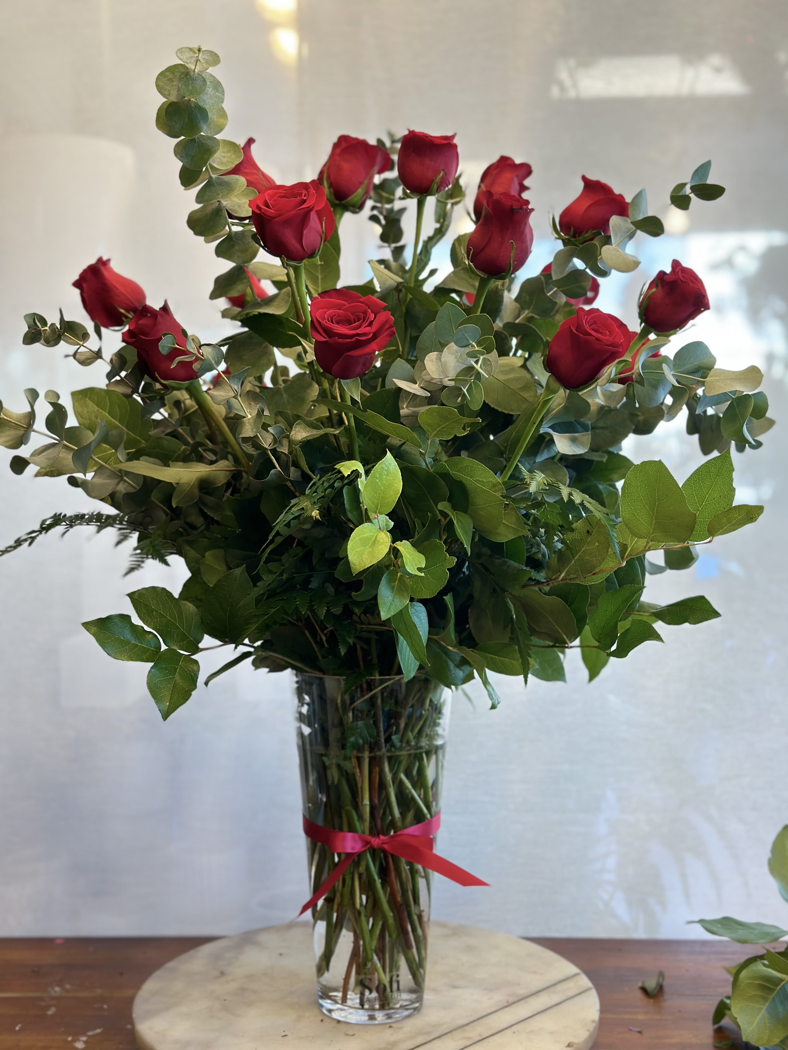 Tall bouquet of red roses in a clear glass vase with a red ribbon