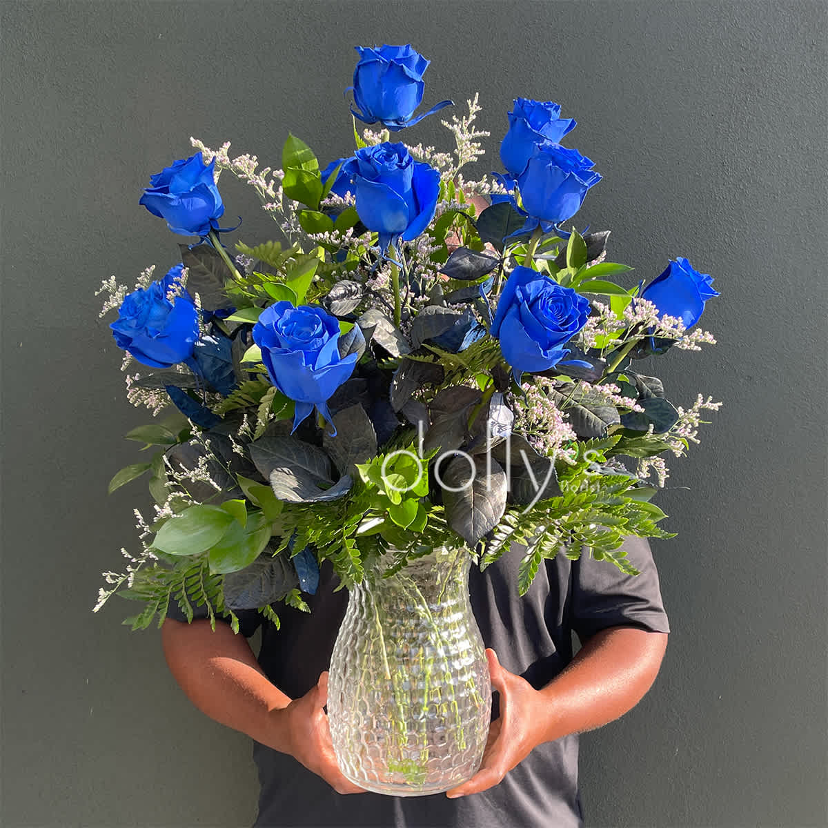Blue roses arranged in a clear glass vase with mixed greenery