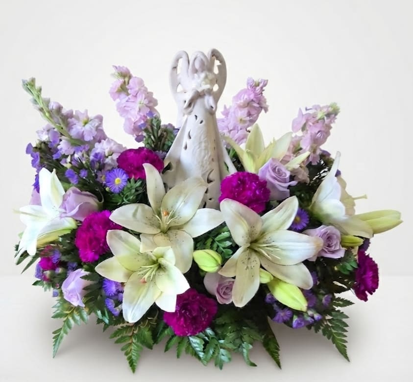 White lilies and purple flowers arranged around a decorative angel figurine