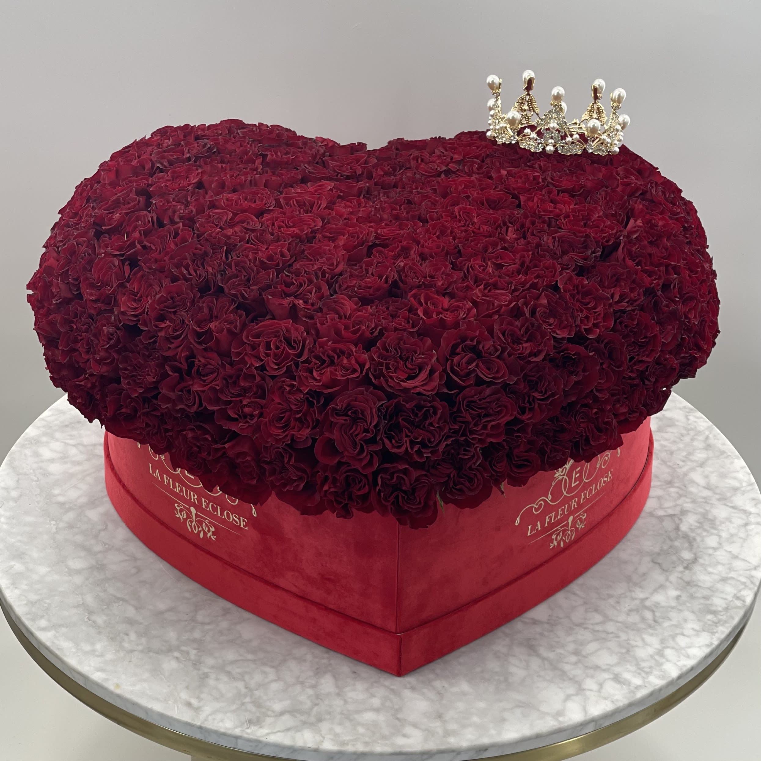 Heart-shaped box of deep red roses with a small crown topper