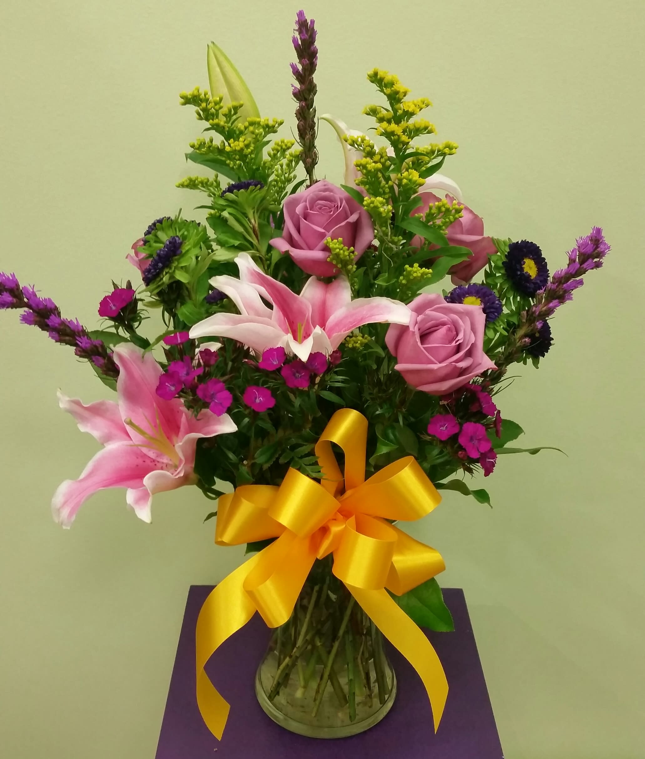 Pink roses and lilies in a glass vase with a yellow ribbon