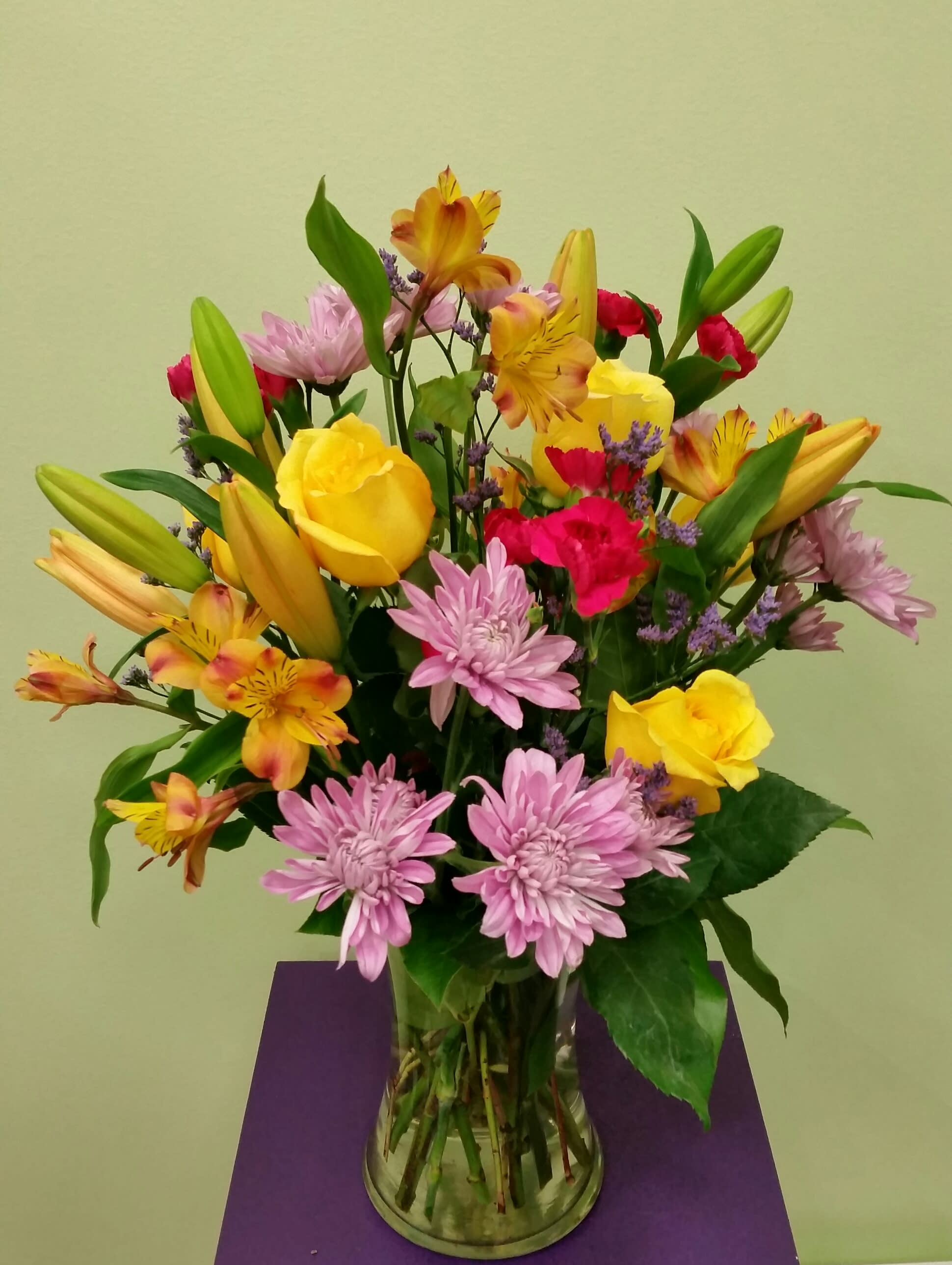 Mixed bouquet of yellow roses, lilies, and pink chrysanthemums in a glass vase