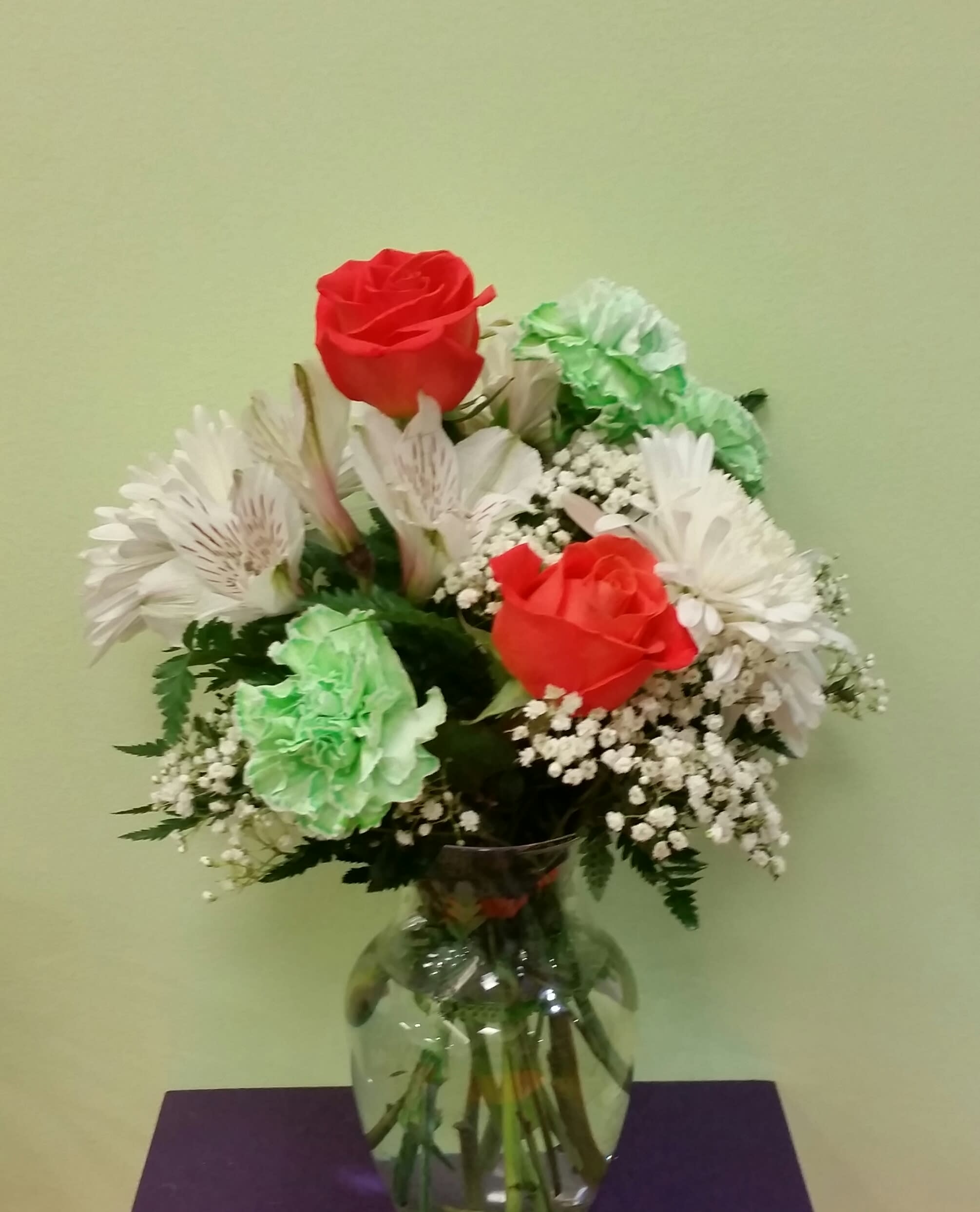 Bouquet of red roses, white daisies, and green carnations in a glass vase