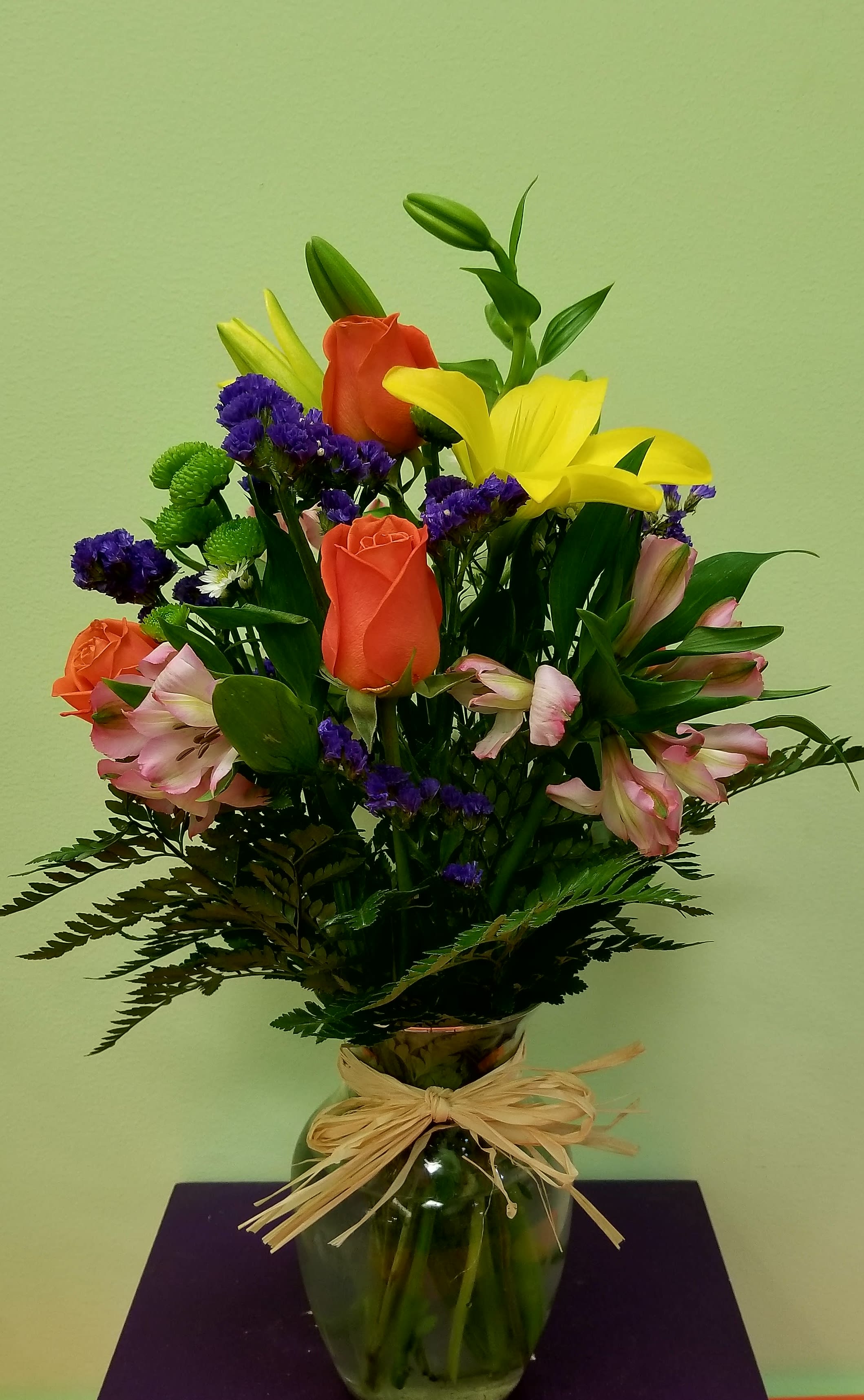 Mixed bouquet of lilies, roses, and purple filler flowers in a glass vase