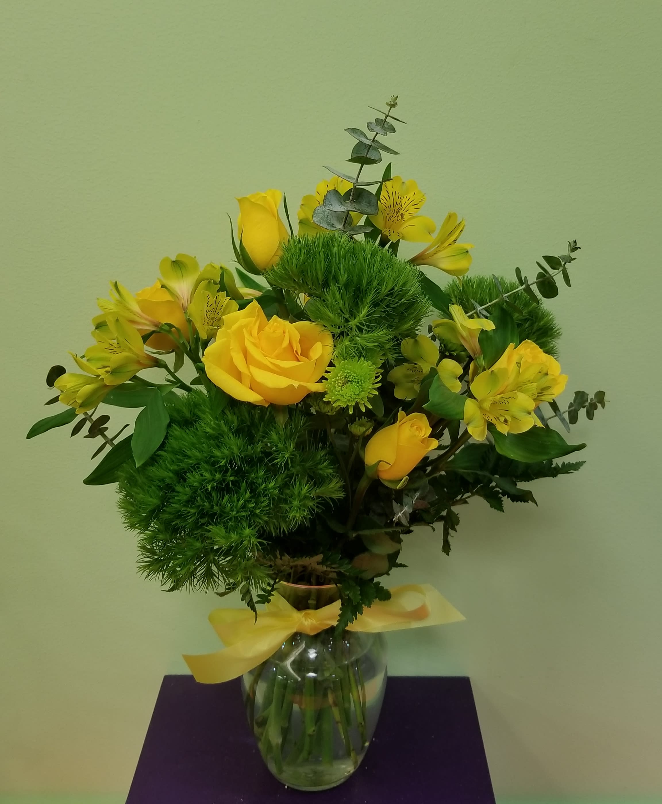 Yellow roses and alstroemeria in a glass vase with a yellow ribbon