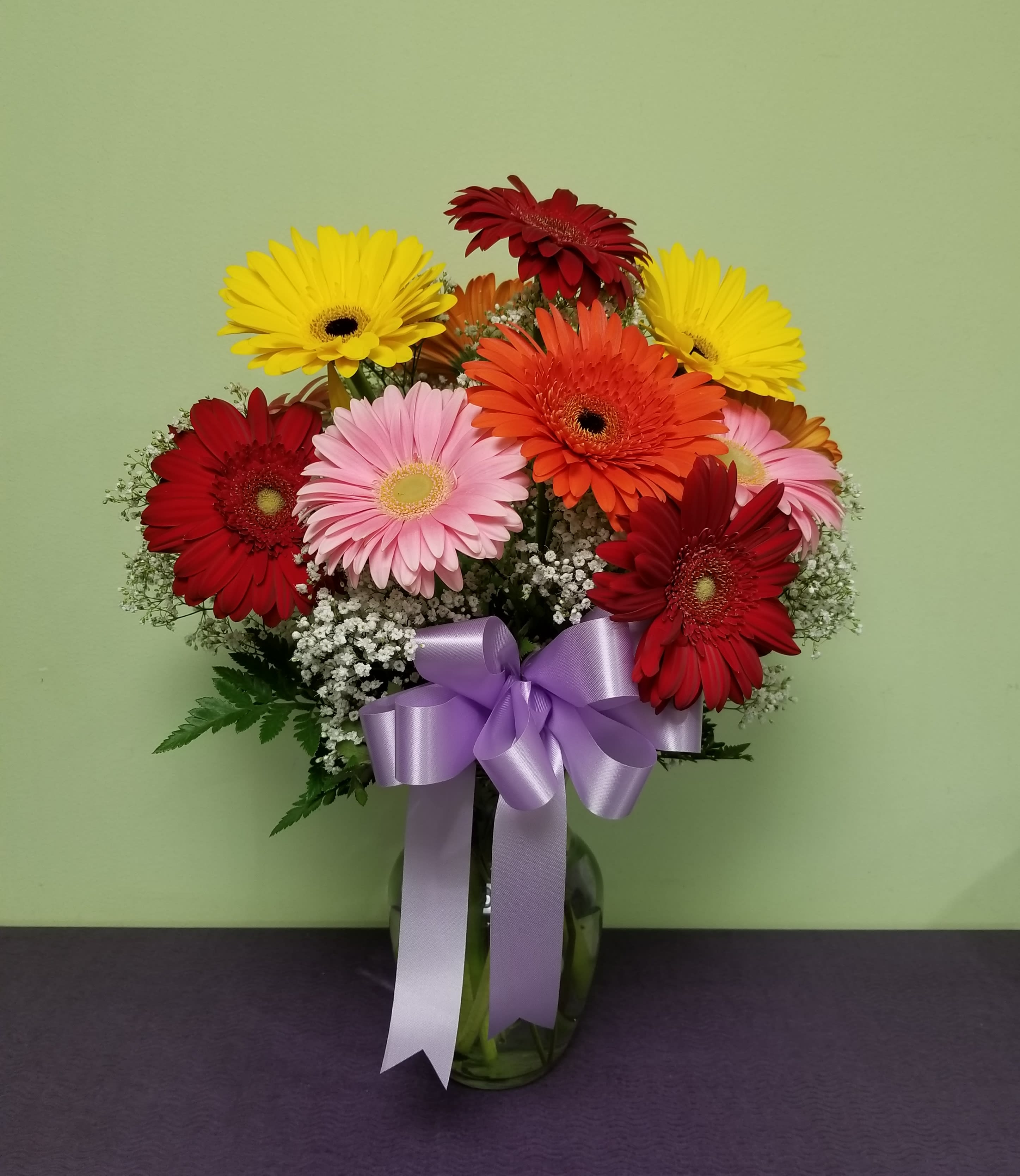 Bouquet of colorful gerbera daisies in a glass vase with a purple ribbon
