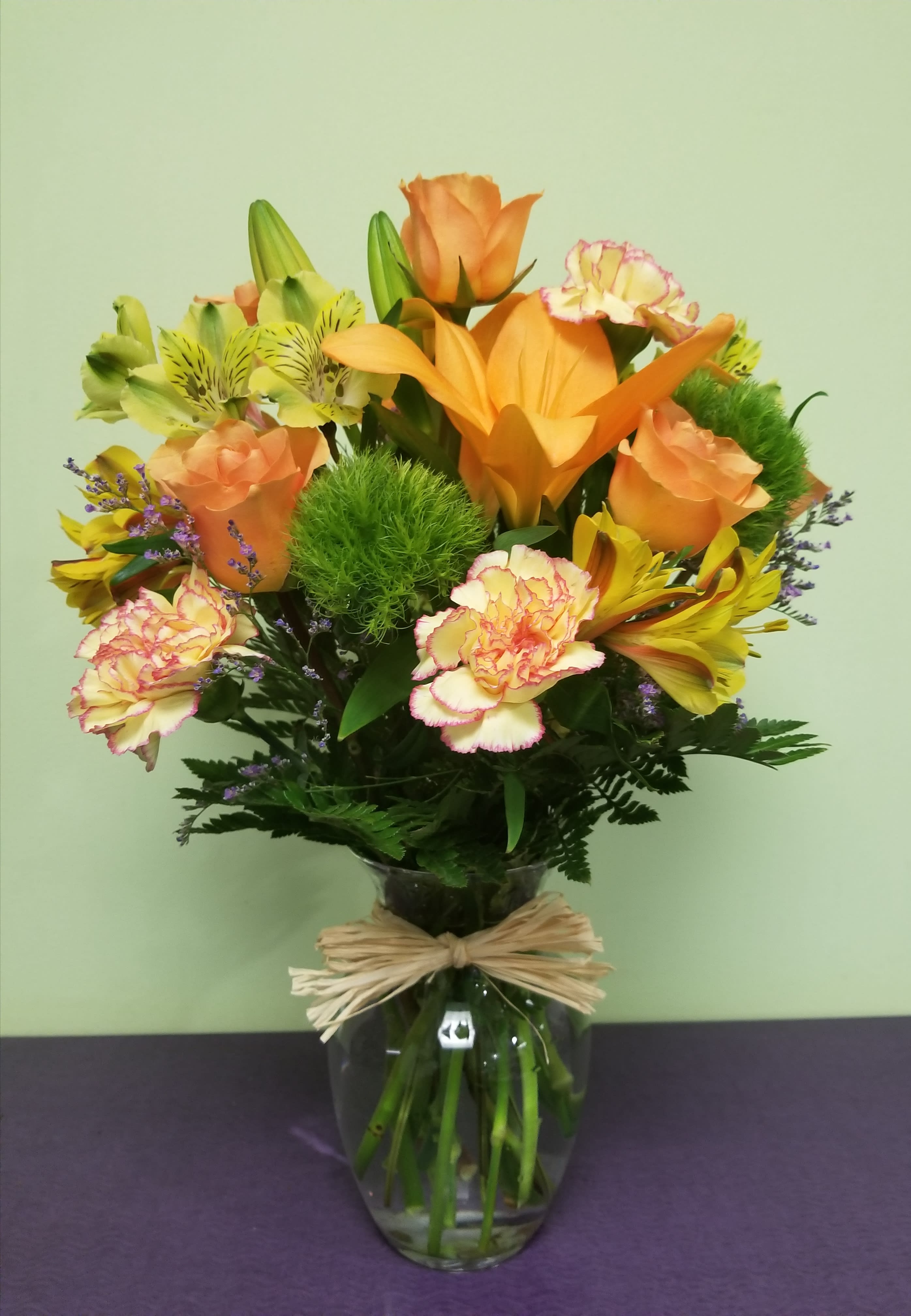 Orange and yellow mixed bouquet in a glass vase with a raffia bow