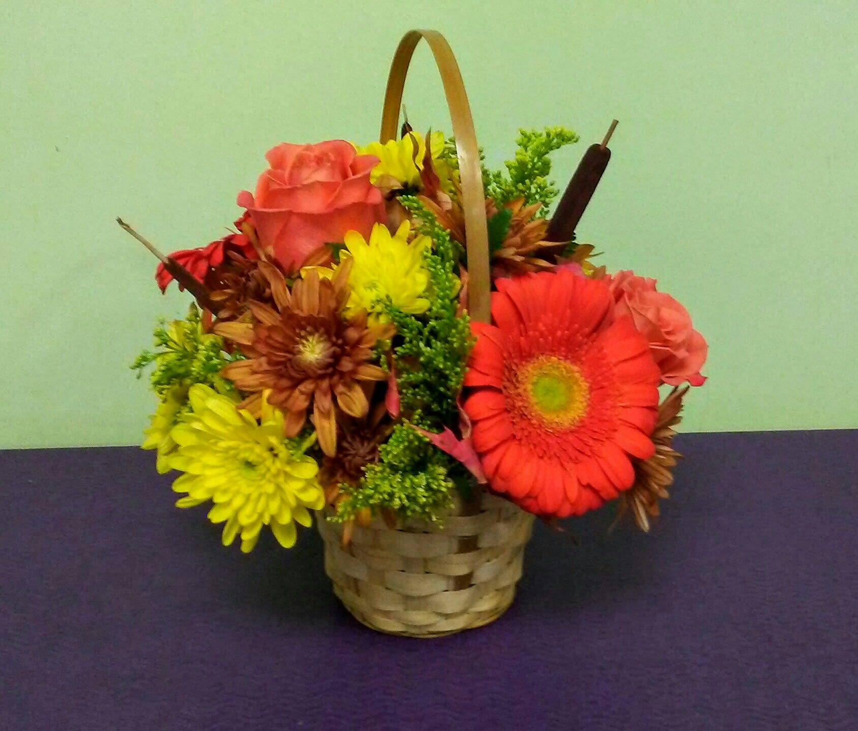 Basket arrangement with pink roses, yellow and orange daisies, and greenery