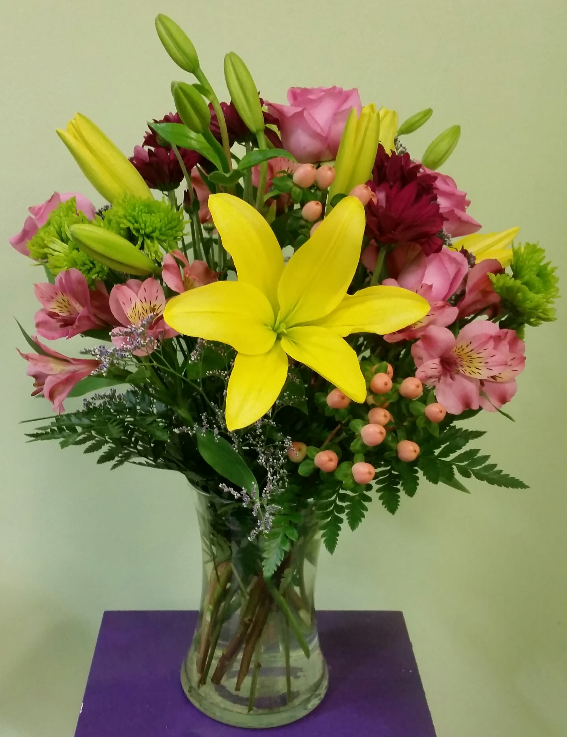 Bouquet of yellow lilies, pink roses, and mixed blooms in a glass vase