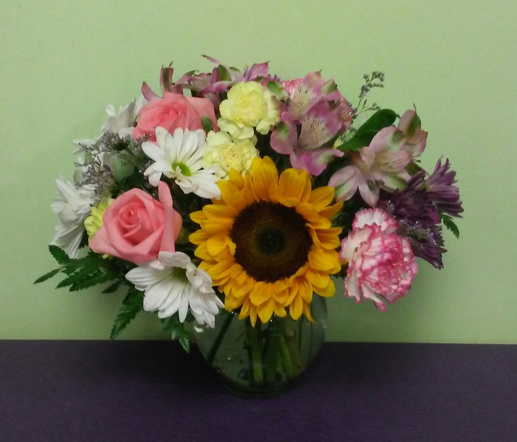 Mixed bouquet with a sunflower, pink roses, and white daisies in a glass vase