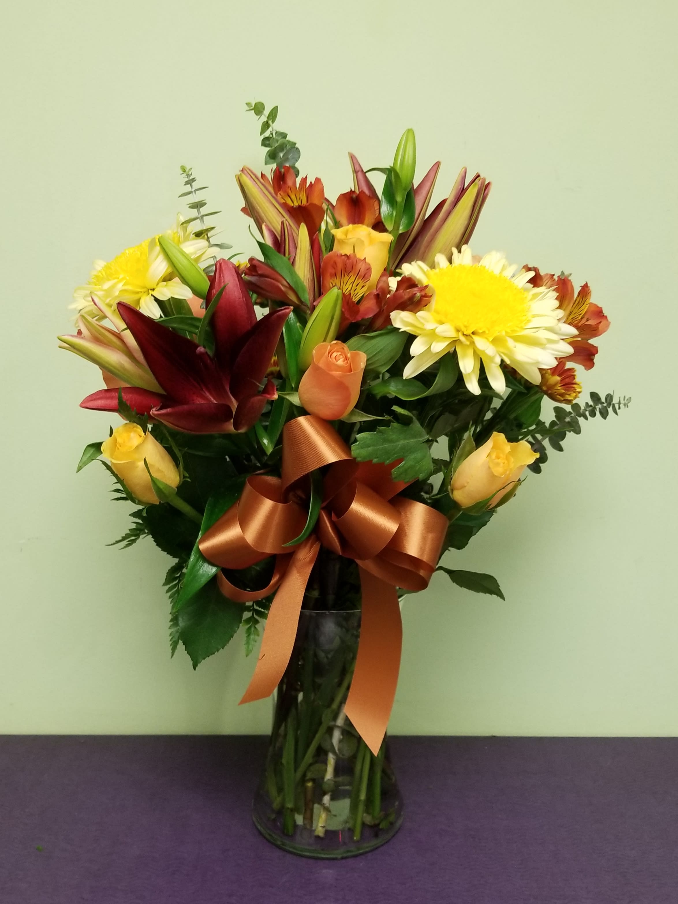 Mixed bouquet of lilies, roses, and daisies in a glass vase with a ribbon