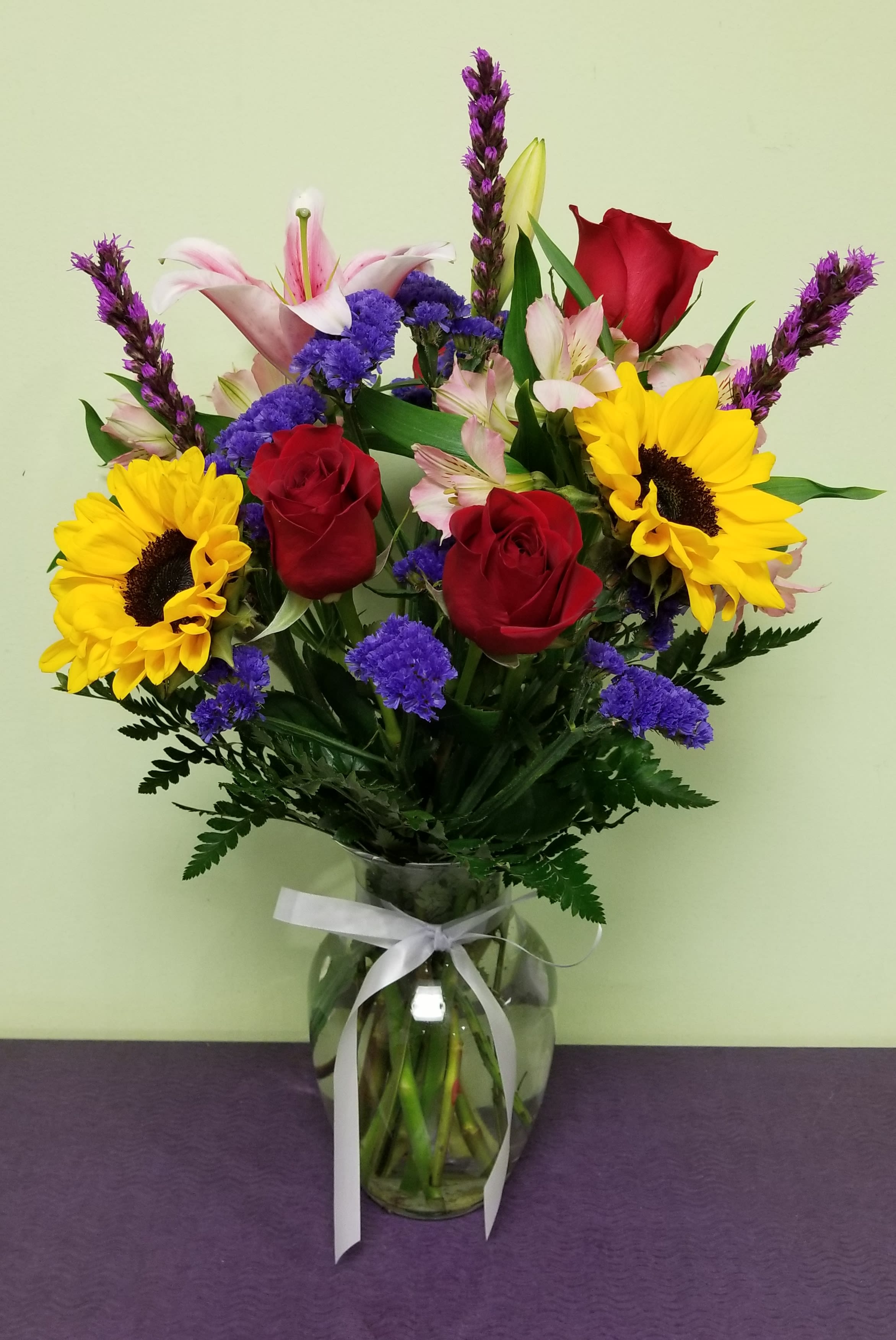 Bouquet of red roses, sunflowers, and pink lilies in a glass vase