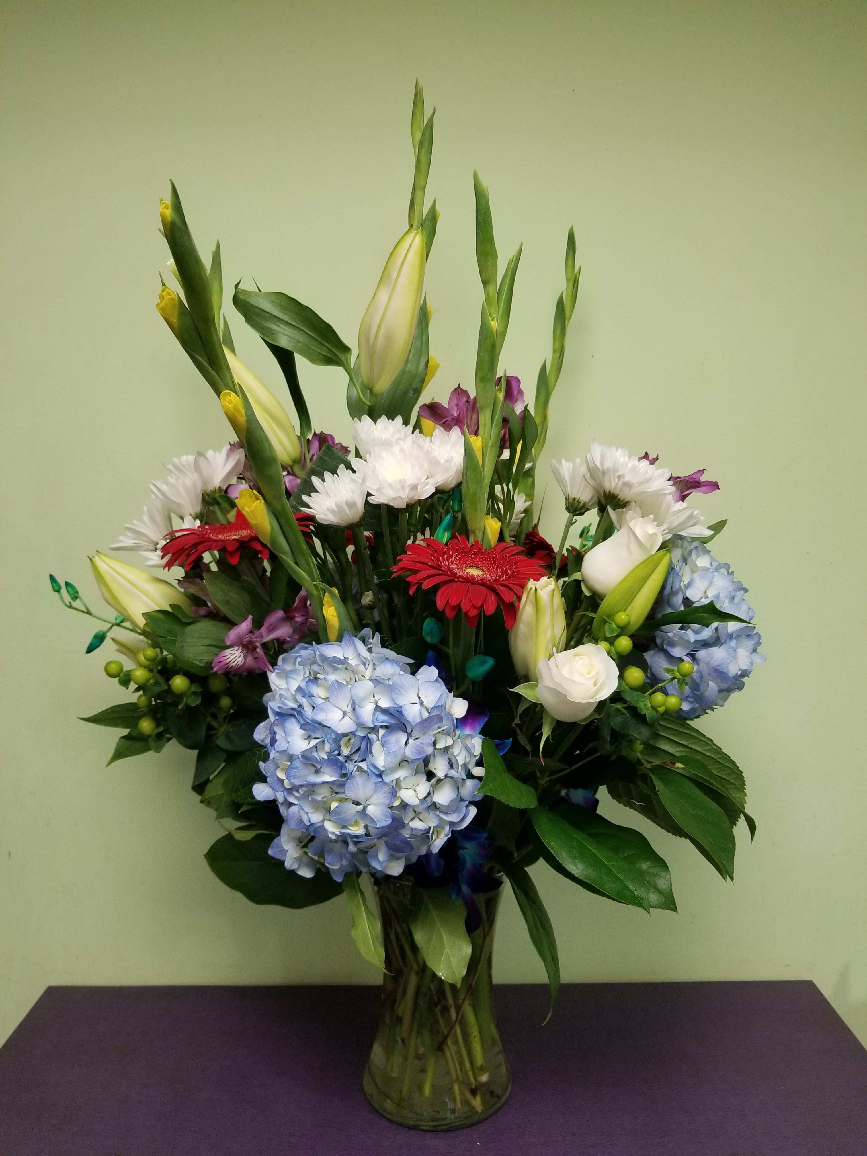 Mixed bouquet in a glass vase with blue hydrangeas, lilies, and gerbera daisies
