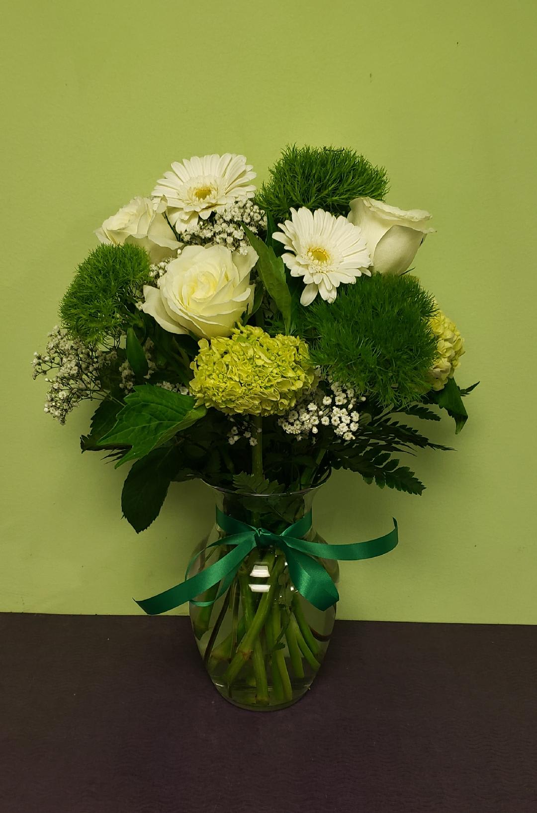 White flowers and green blooms arranged in a glass vase with a ribbon