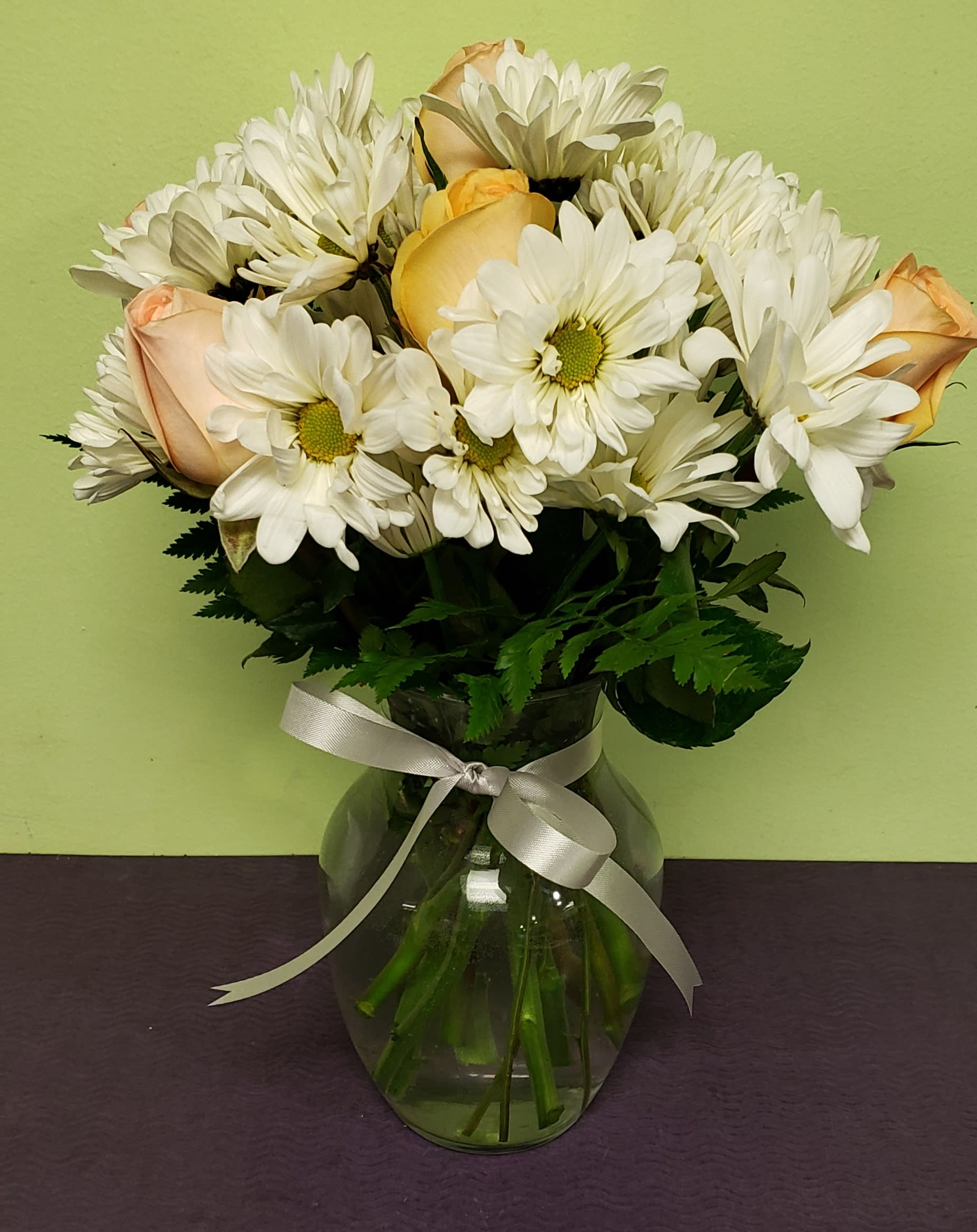 White daisies and pale peach roses in a glass vase with a ribbon