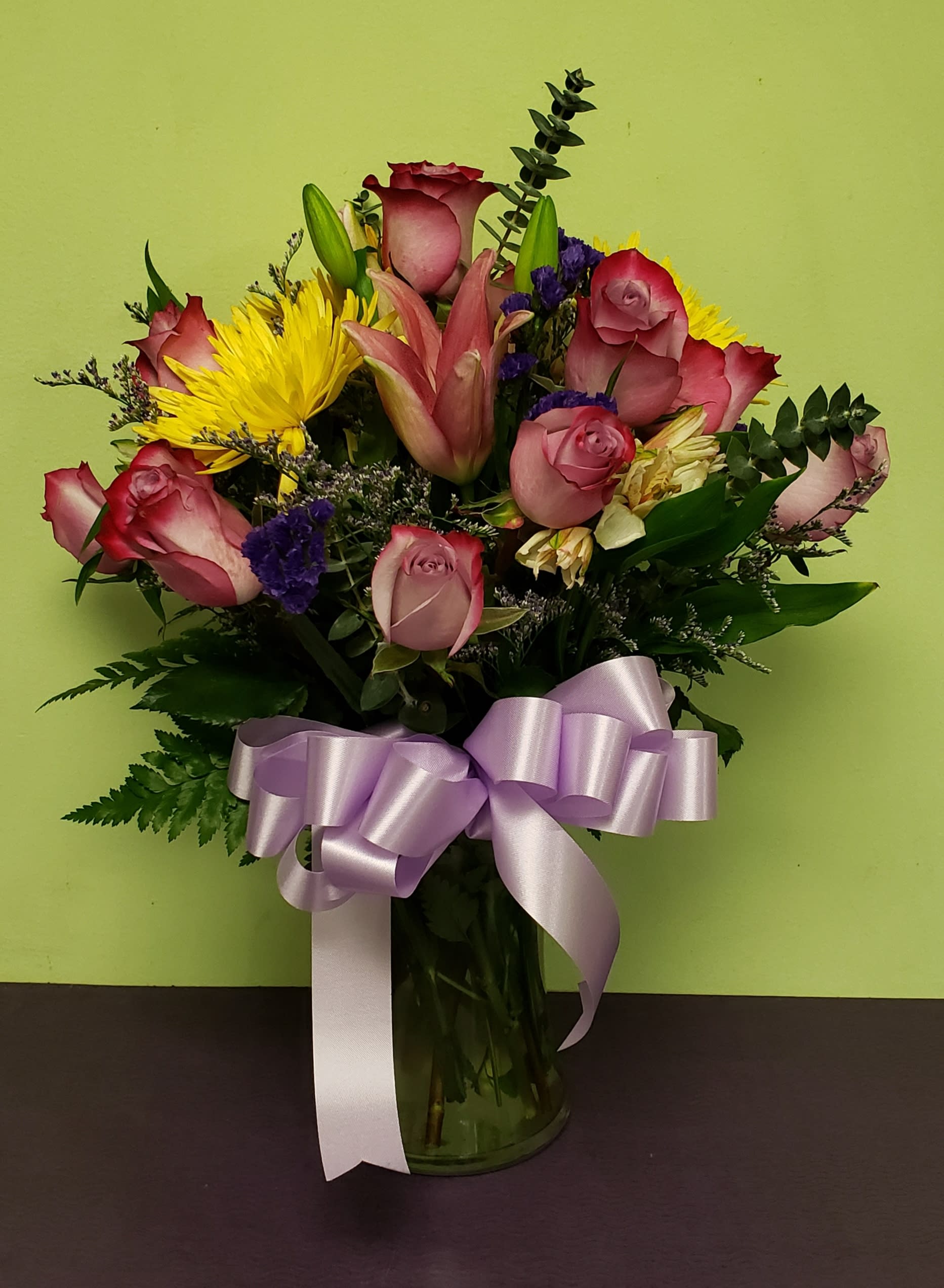 Bouquet of pink roses and yellow lilies in a glass vase with a lavender ribbon