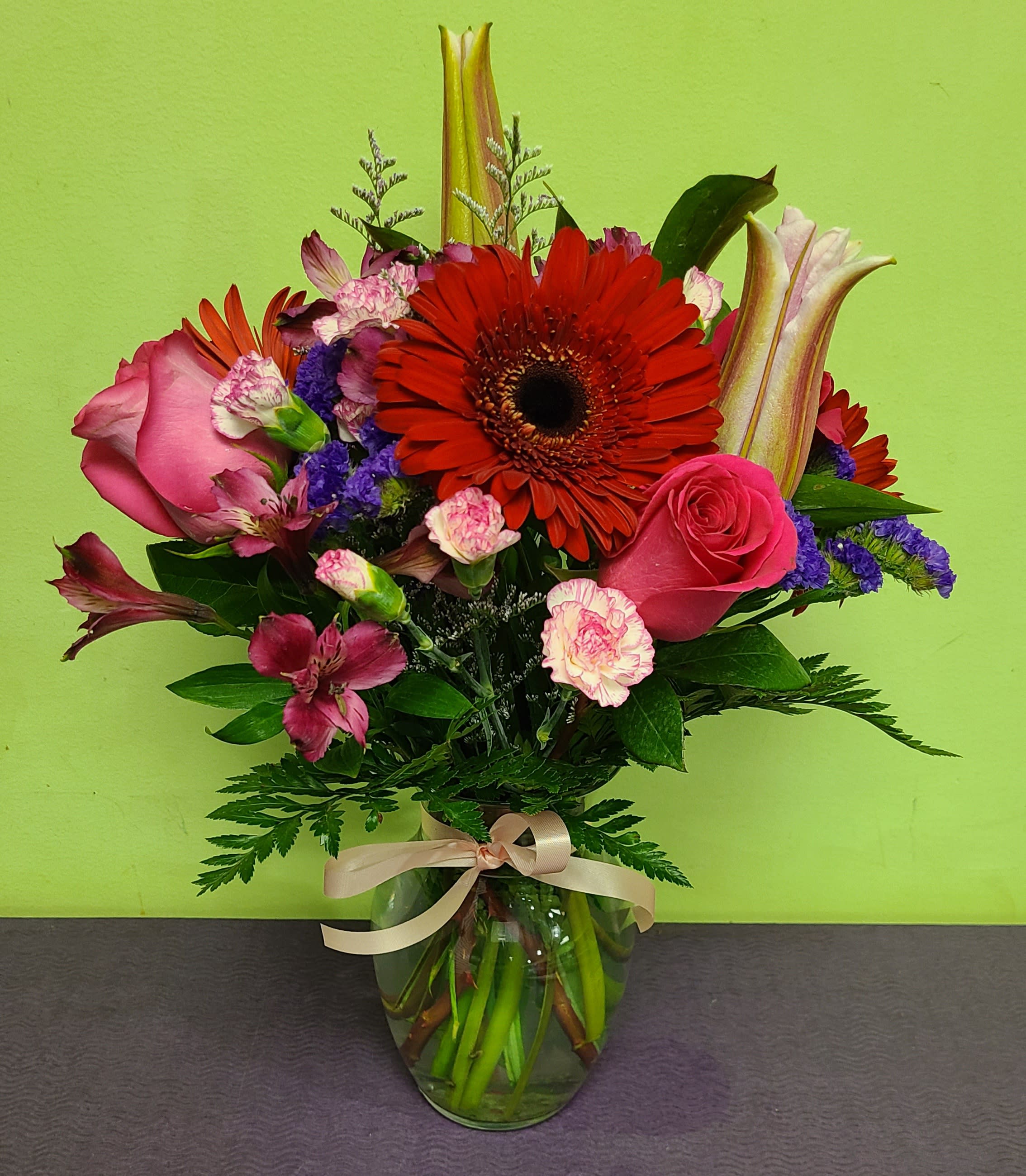 Mixed bouquet with pink roses, red gerbera daisies, and lilies in a glass vase