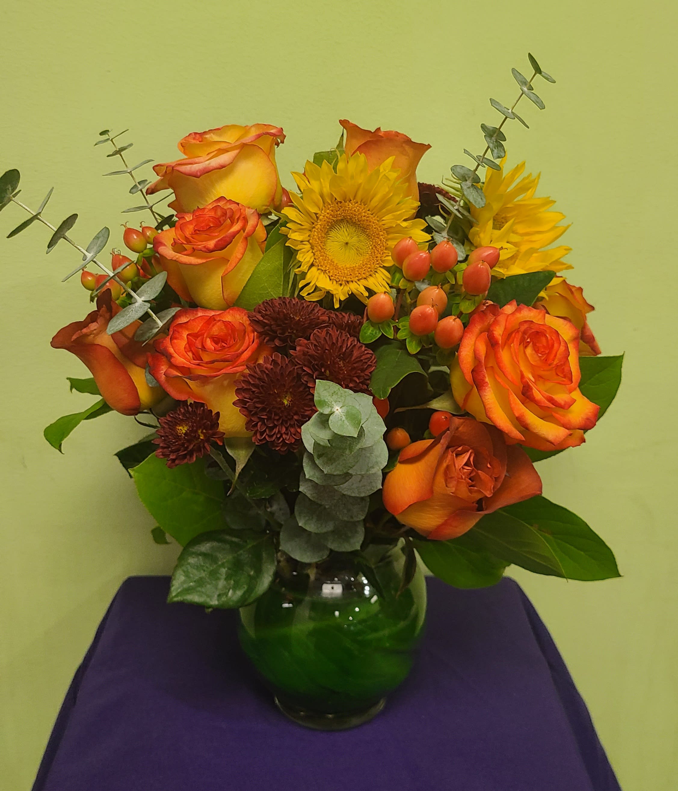 Orange and yellow roses with sunflowers in a glass vase