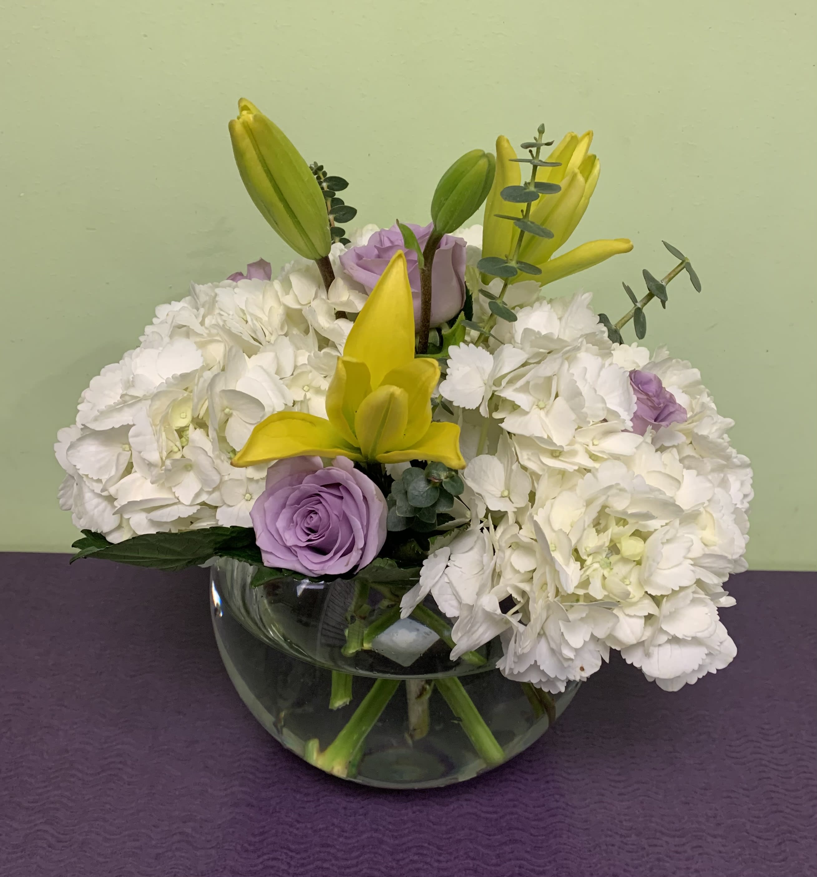 White hydrangeas with yellow lilies and lavender roses in a glass bowl vase