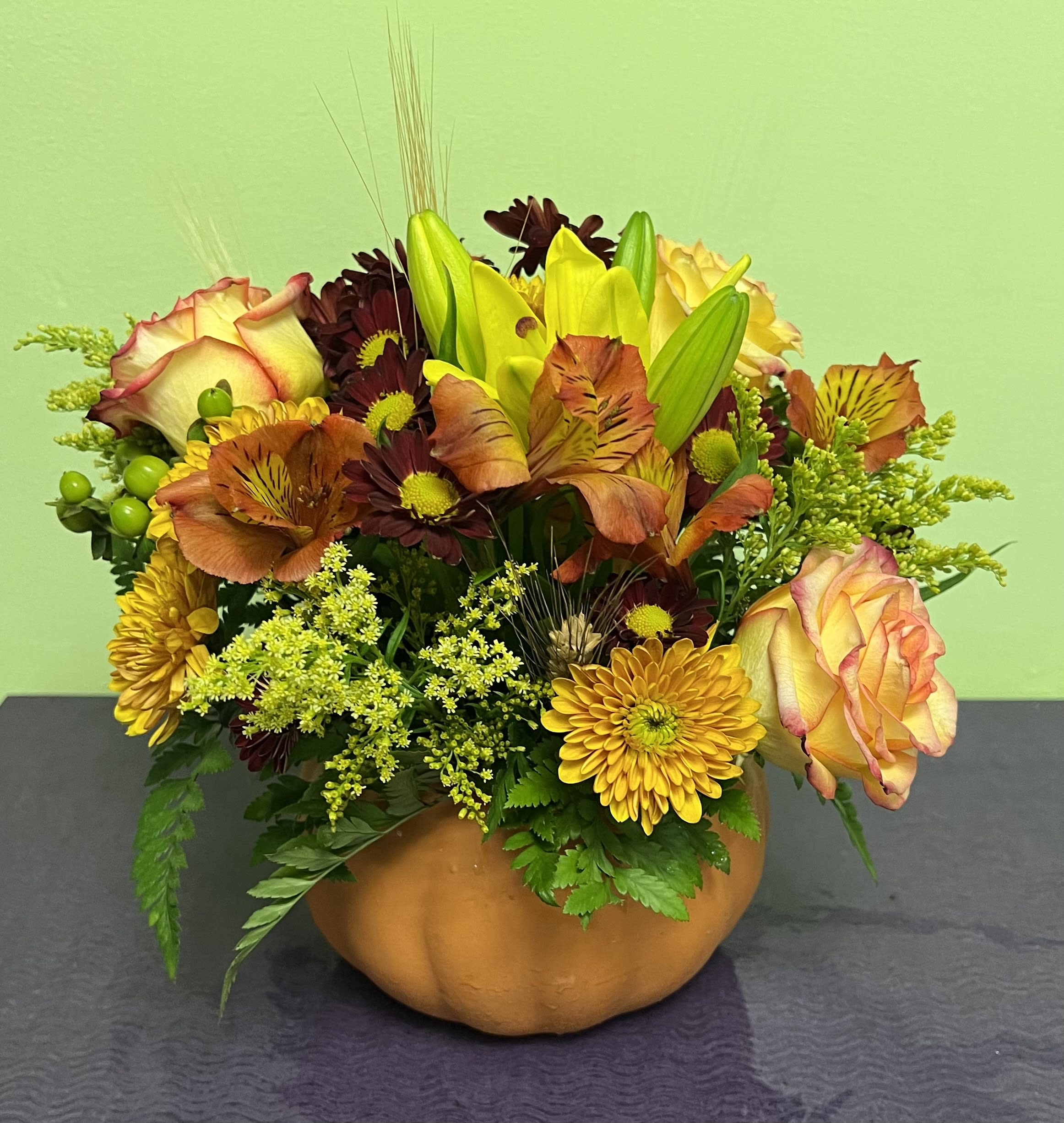 Autumn floral arrangement in a pumpkin-shaped container with roses and lilies