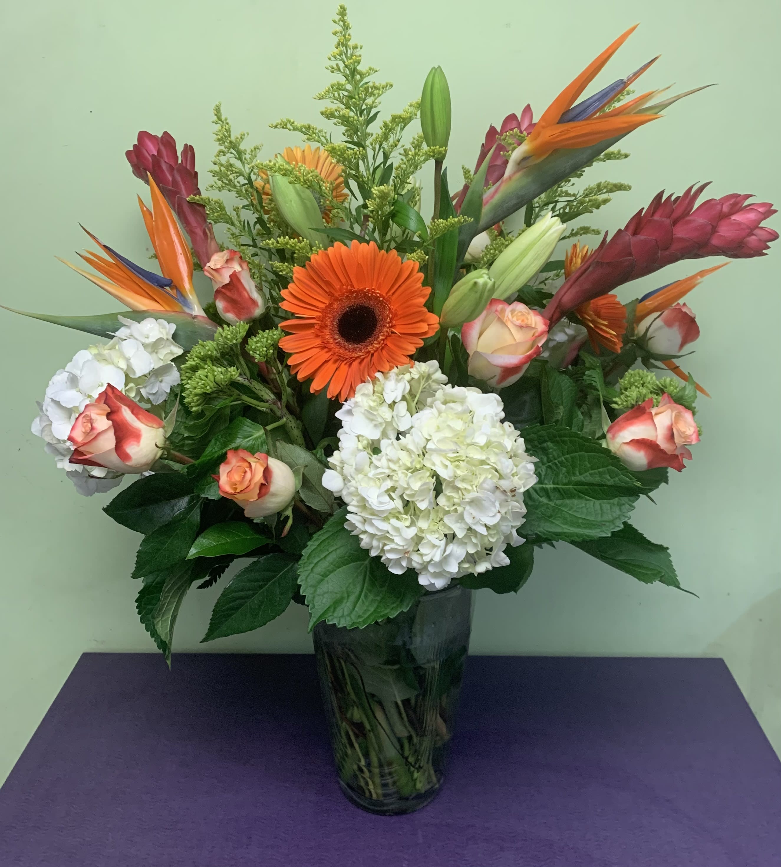 Tropical bouquet with orange gerbera daisies, roses, and white hydrangeas in a glass vase