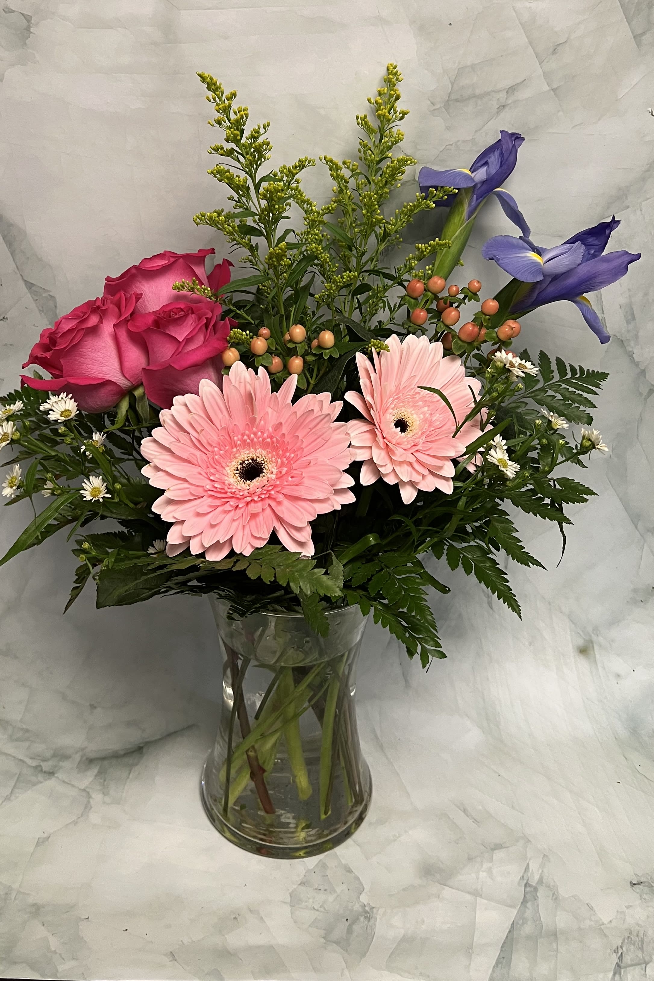 Pink roses and gerbera daisies in a clear glass vase with purple irises