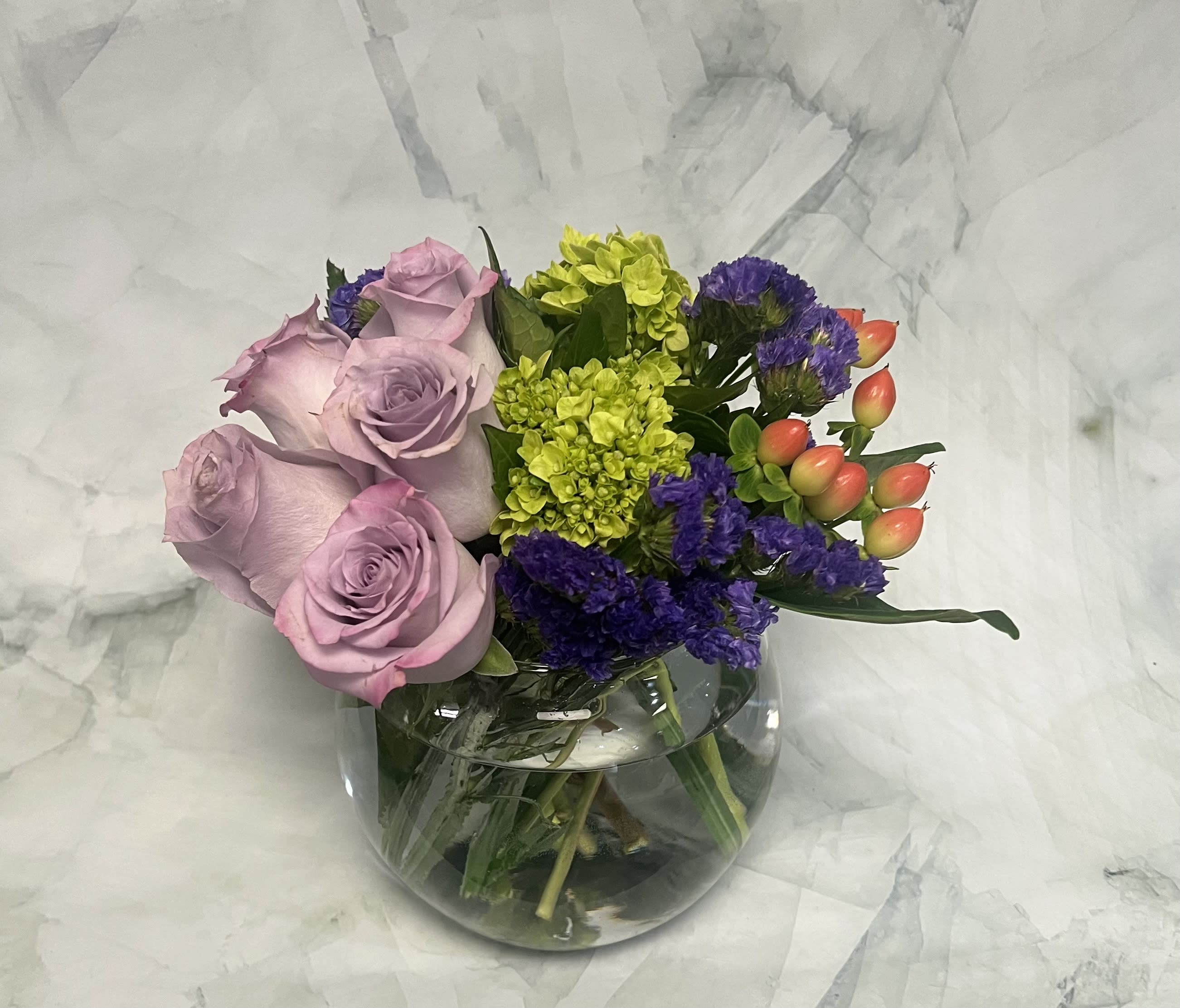 Lavender roses with purple and lime-green flowers in a glass vase