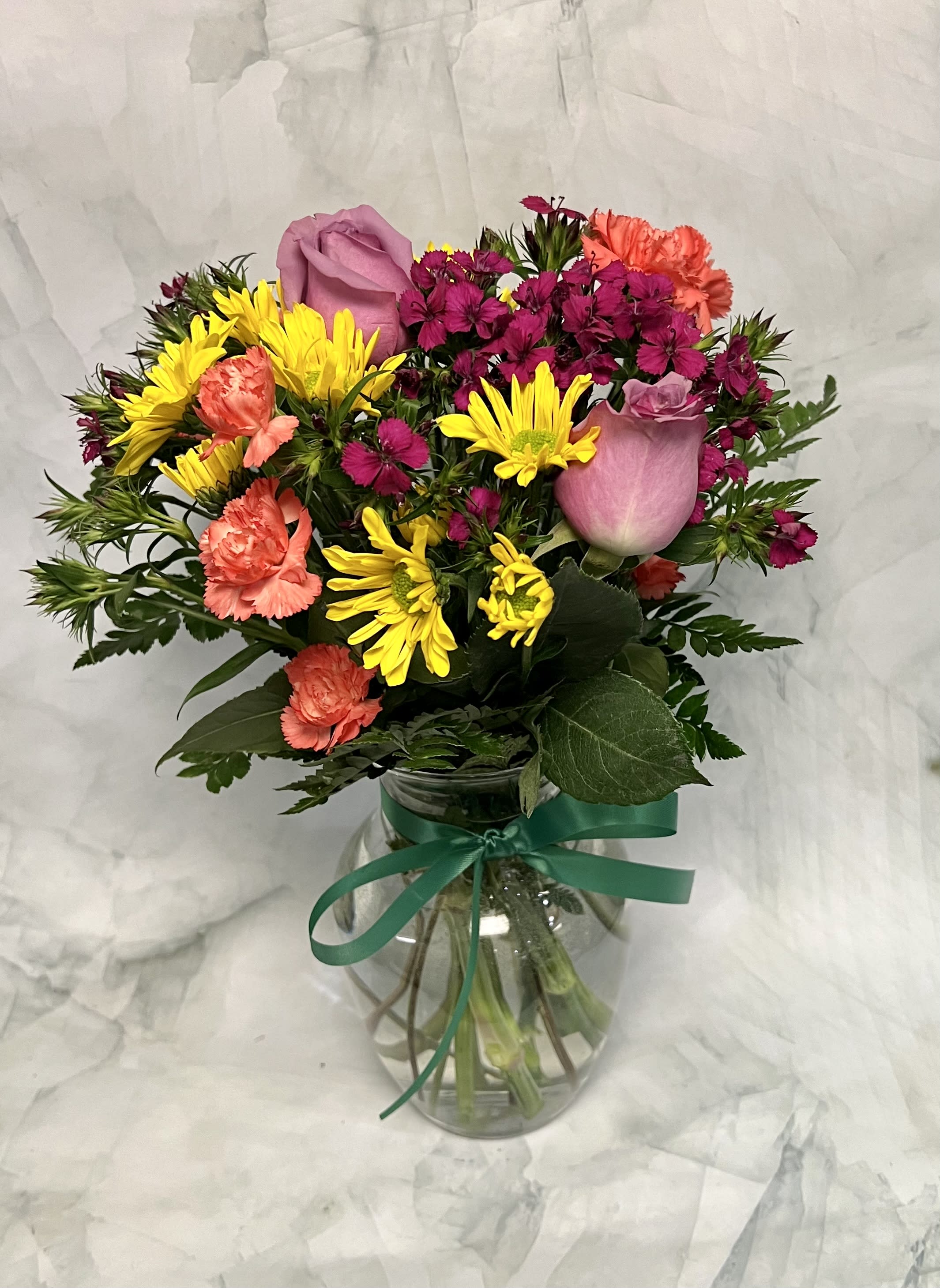Mixed bouquet of pink roses, yellow daisies, and coral carnations in a glass vase