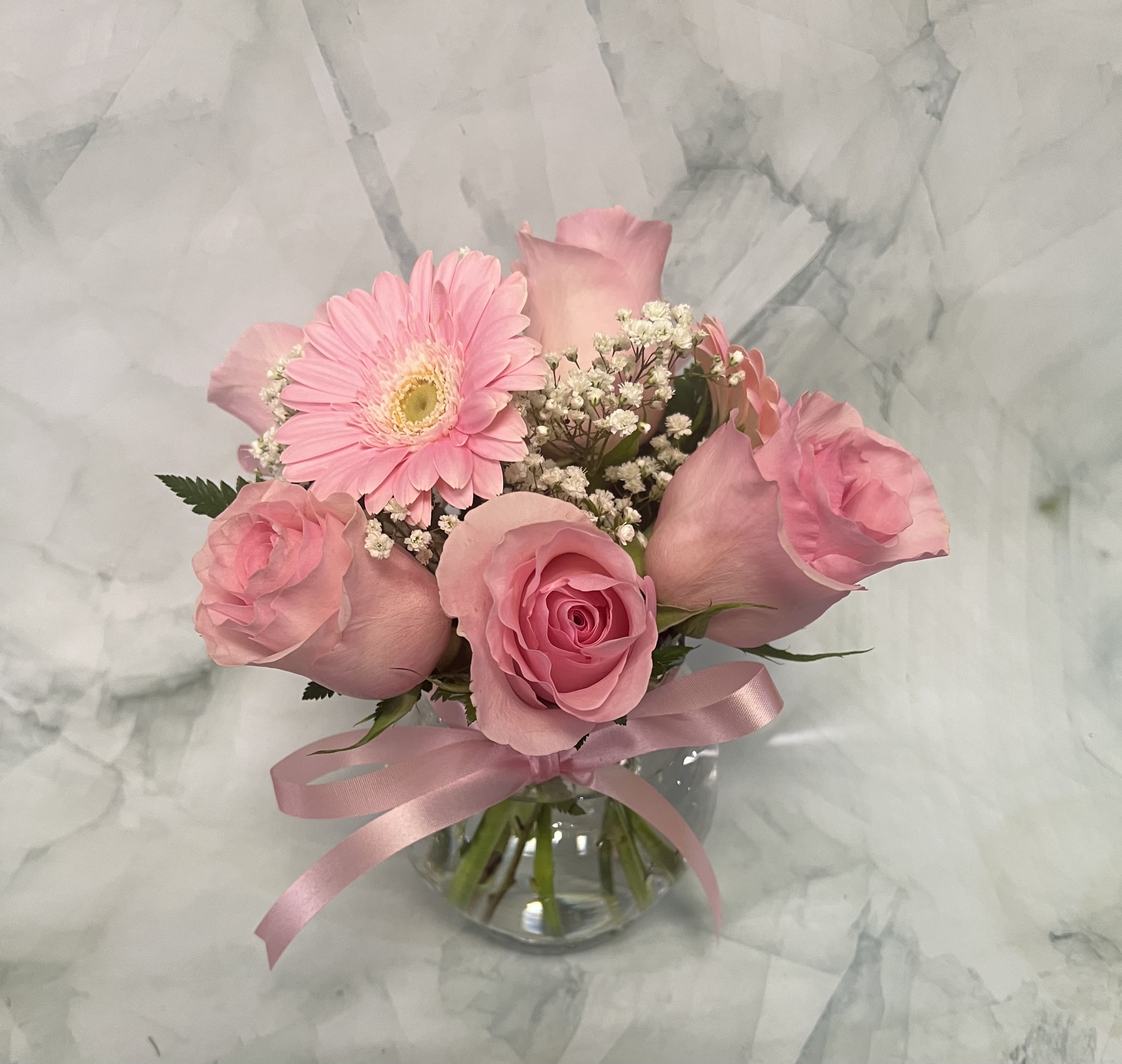 Pink roses and a gerbera daisy in a glass vase with a pink ribbon