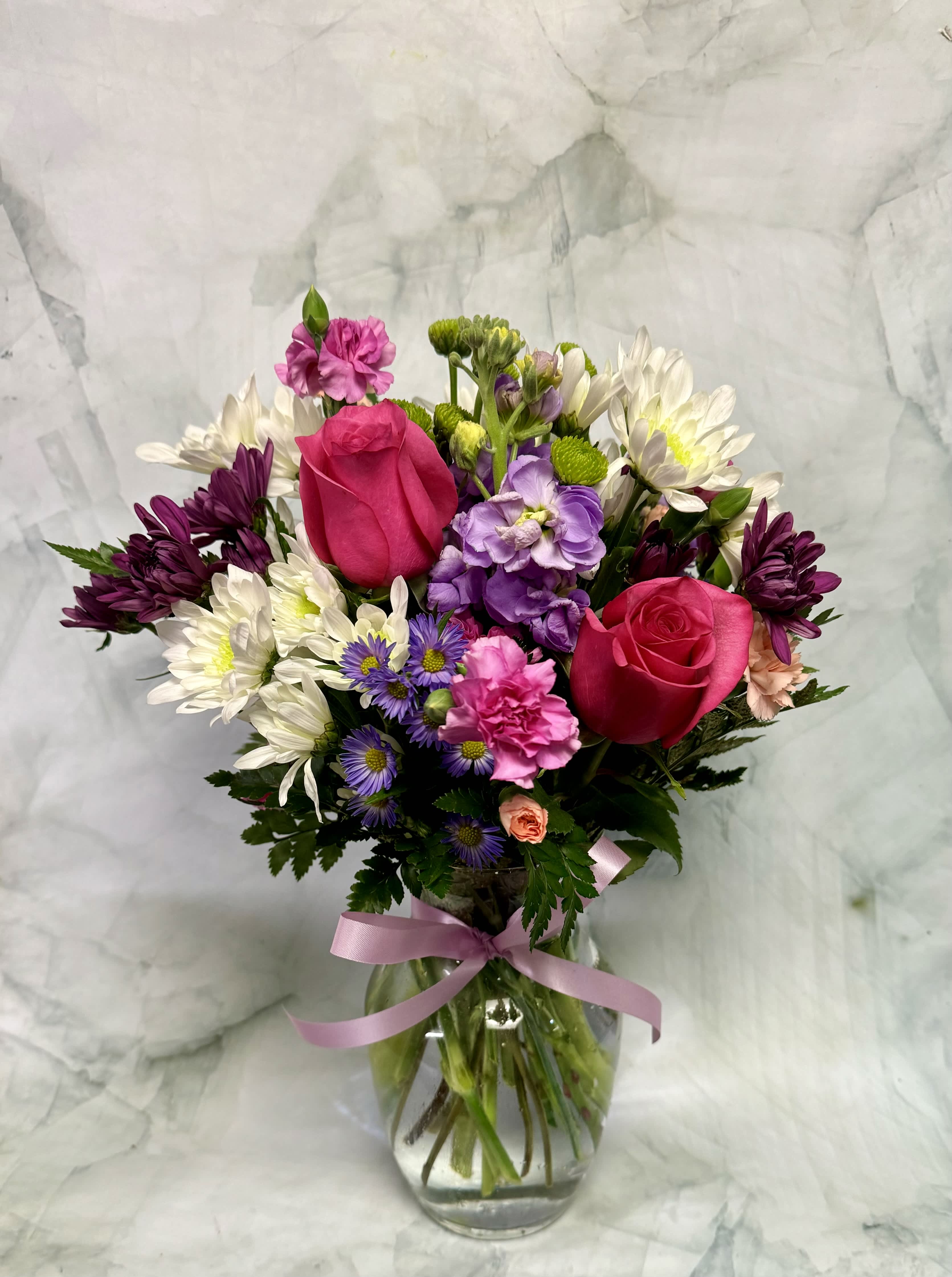 Mixed bouquet of pink roses, purple flowers, and white daisies in a glass vase
