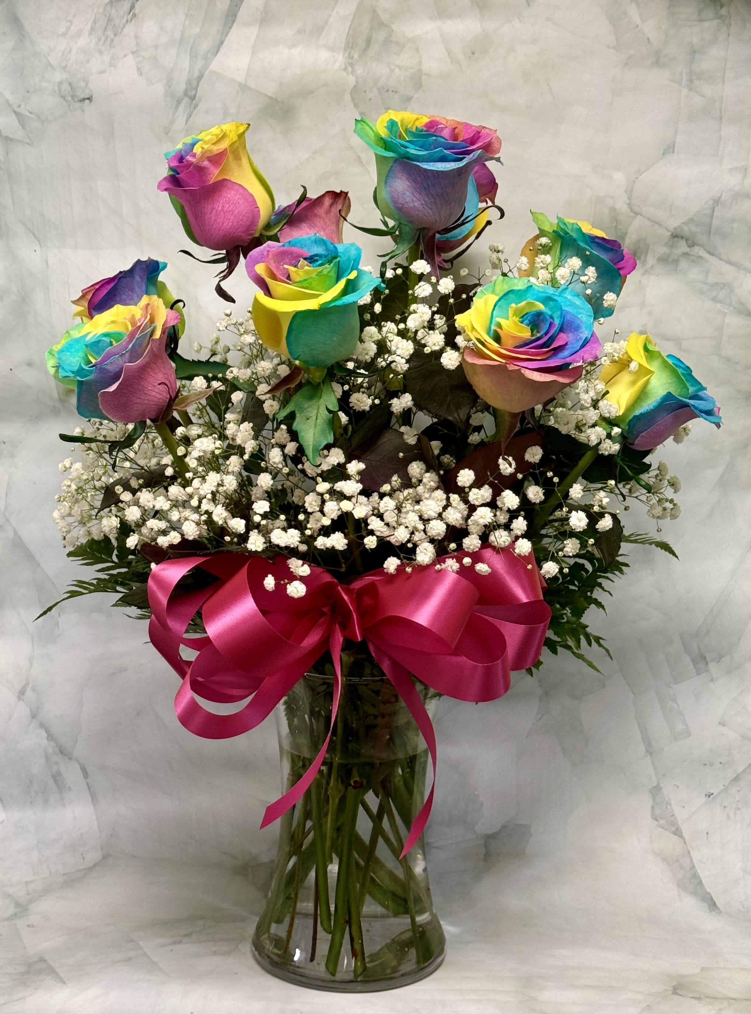 Rainbow-colored roses in a glass vase with a pink ribbon