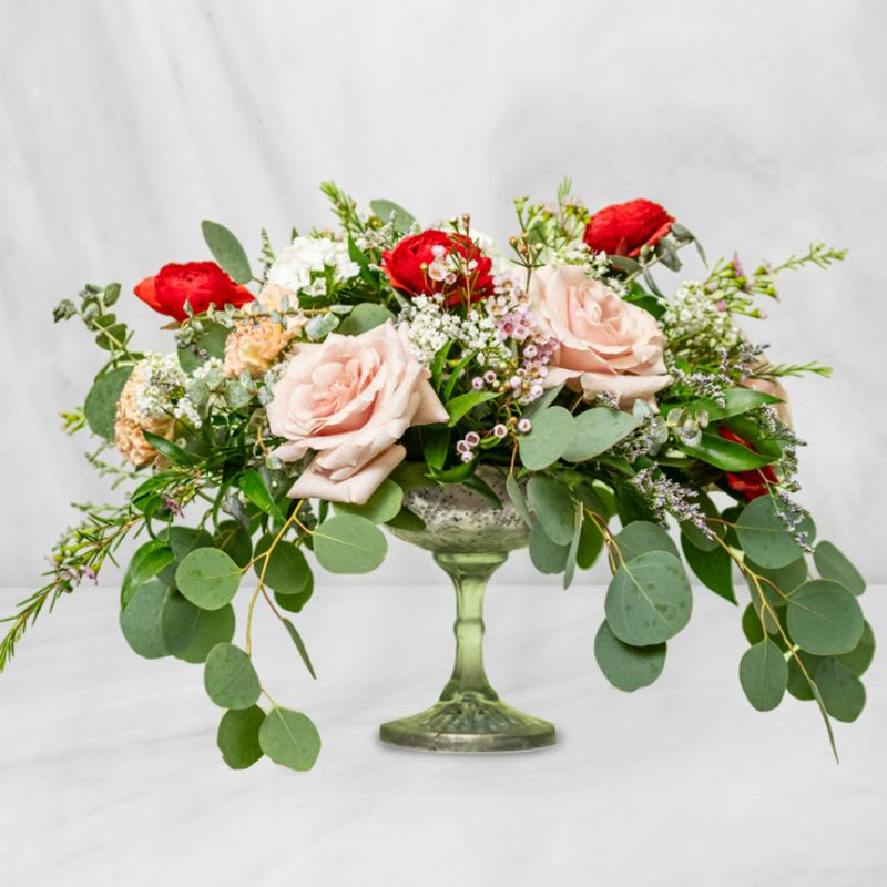 Low floral arrangement in a green glass pedestal vase with pink and red roses